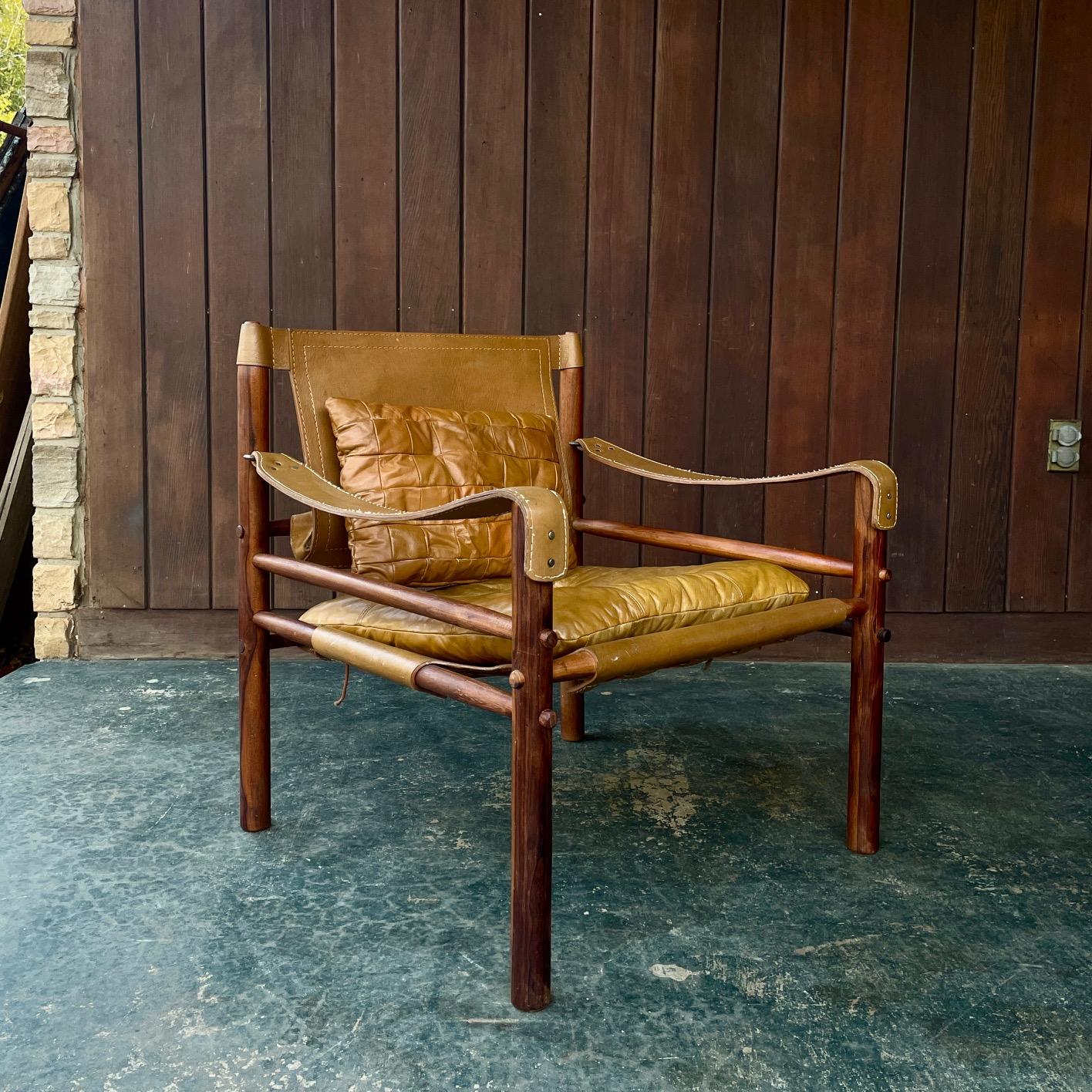 The Sirocco safari chair designed by Arne Norell in 1966. This example is in camel-colored leather; with two cushions and slings with brass fittings. Designed to breakdown for flat pack shipping or Camping on the Serengeti.

Missing the brass strap