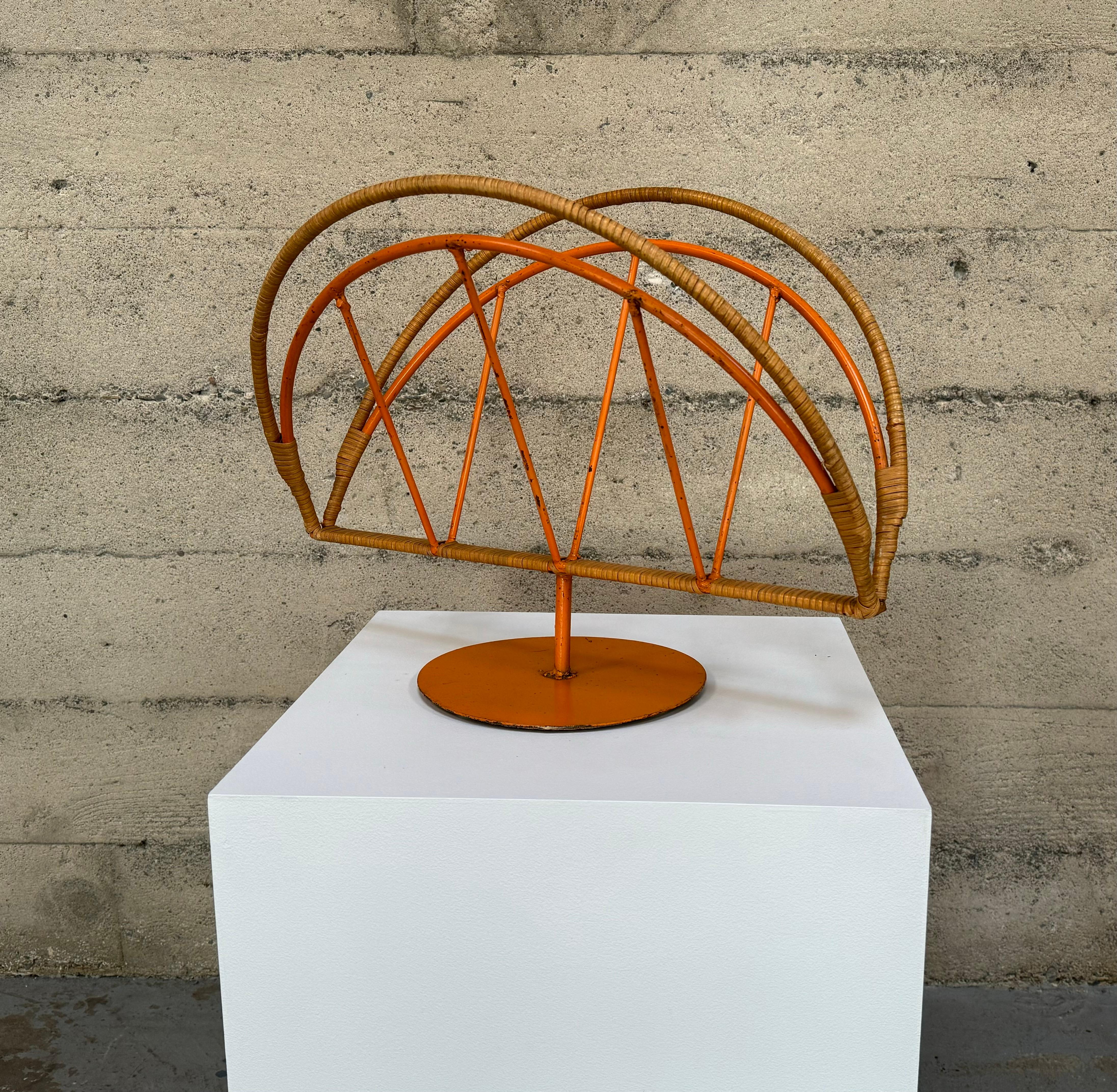 1960s welded cane wrapped iron magazine holder painted in a salmon lacquer. Double arched form with cross bars running within the arch resting on a round base. Arthur Umanoff was a New York designer in the early 1950s into the 1960s who had a