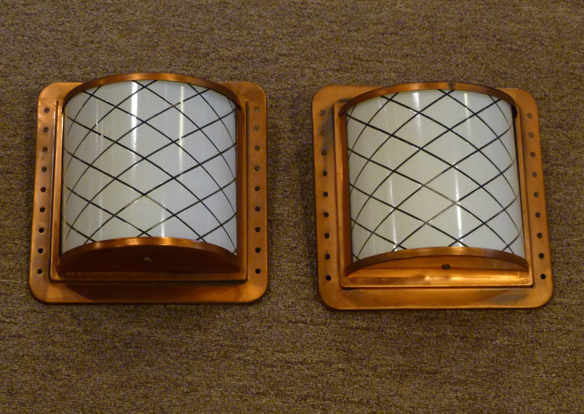 With a Arts & Crafts styling, this pair of antiqued copper and black finished wall lights or sconces from the 1960s, feature a curved glass diffuser with a white lattice design. Each with a new UL single medium base porcelain socket and new wiring.