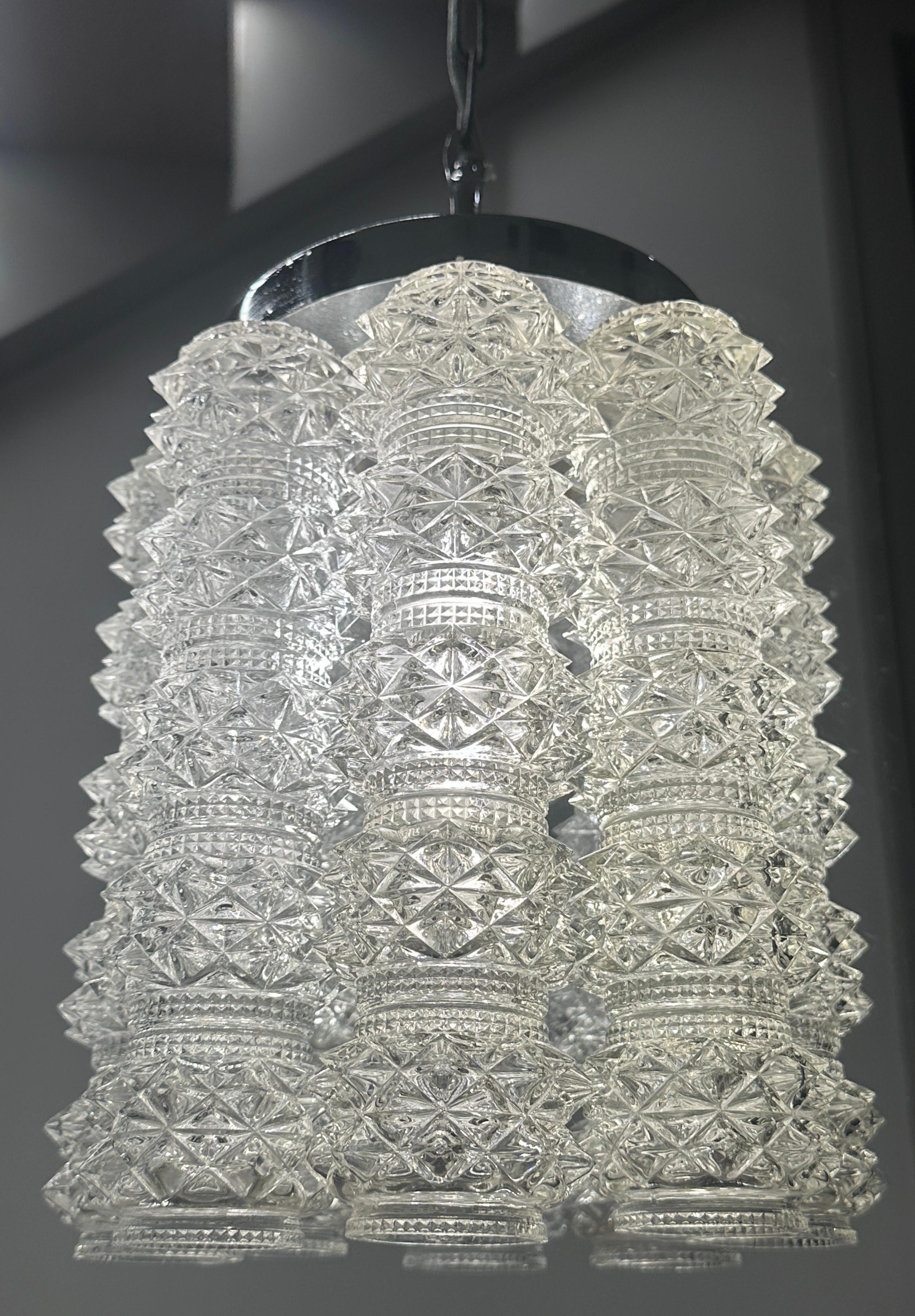 Araña austriaca de los años 60 diseñada por J.T. Kalmar para Kalmar Lighting.  Una llamativa y elegante lámpara de araña con tubos de cristal facetado texturizado suspendidos de una estructura de metal cromado.  Los ocho tubos de cristal