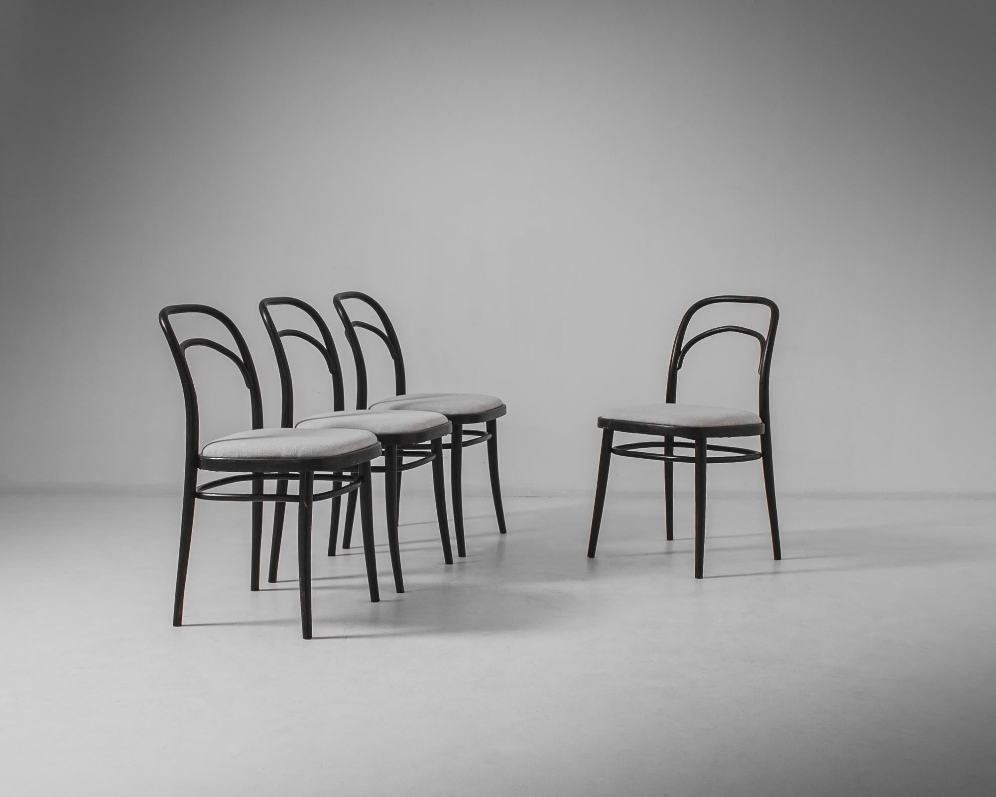 A set of four wooden dining chairs from 1960s Austria. The light, elegant shape, with its curved backrest and subtly tapered legs, is evocative of the bentwood designs of Thonet. The wooden frame is painted a stylish black; a cushioned seat,
