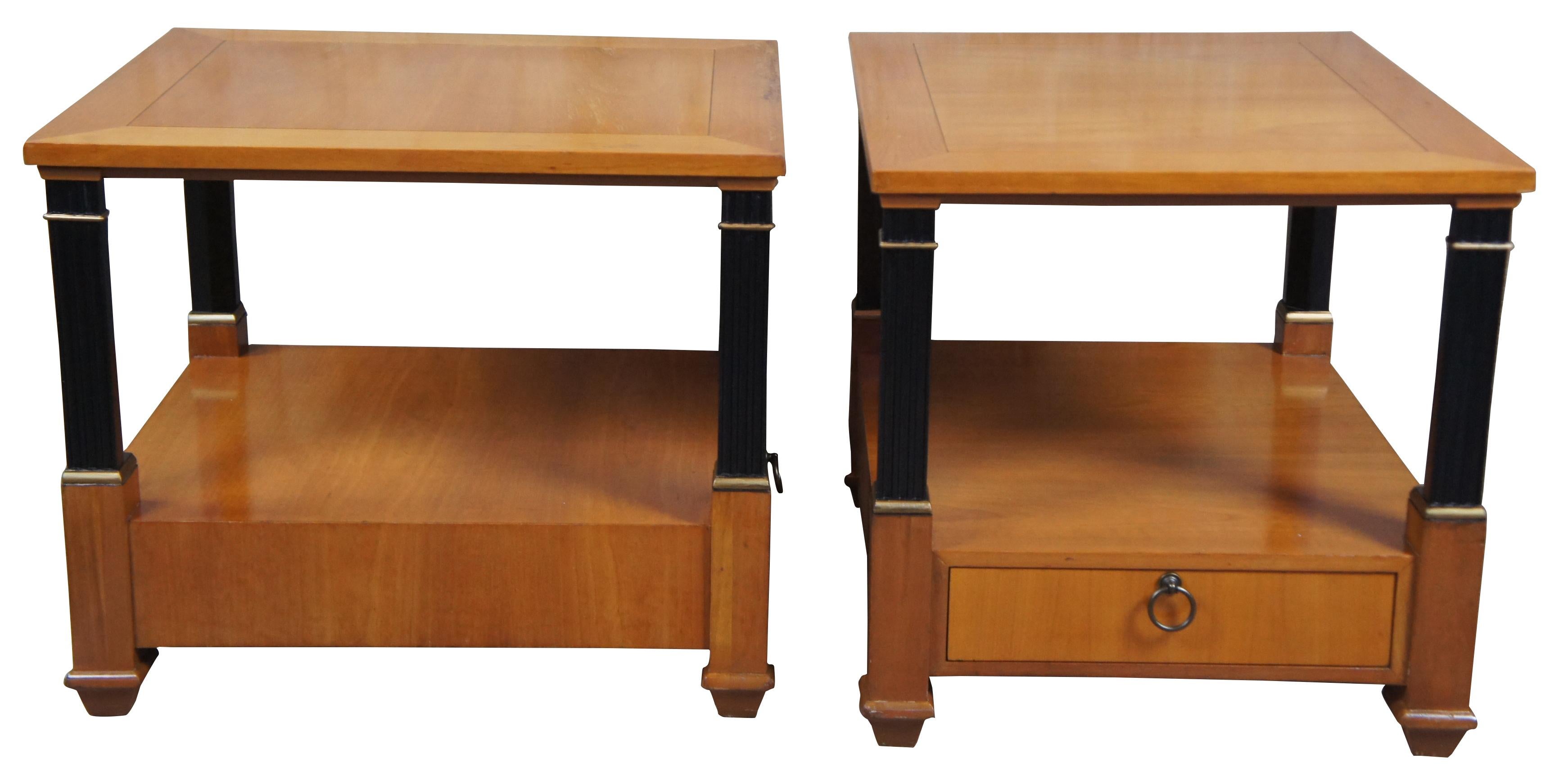 Baker Furniture French Empire fruitwood side tables, circa 1960s. Feature a two tier design supported by ebonized columns with gold trim. Includes lower drawer with knocker pull.
 