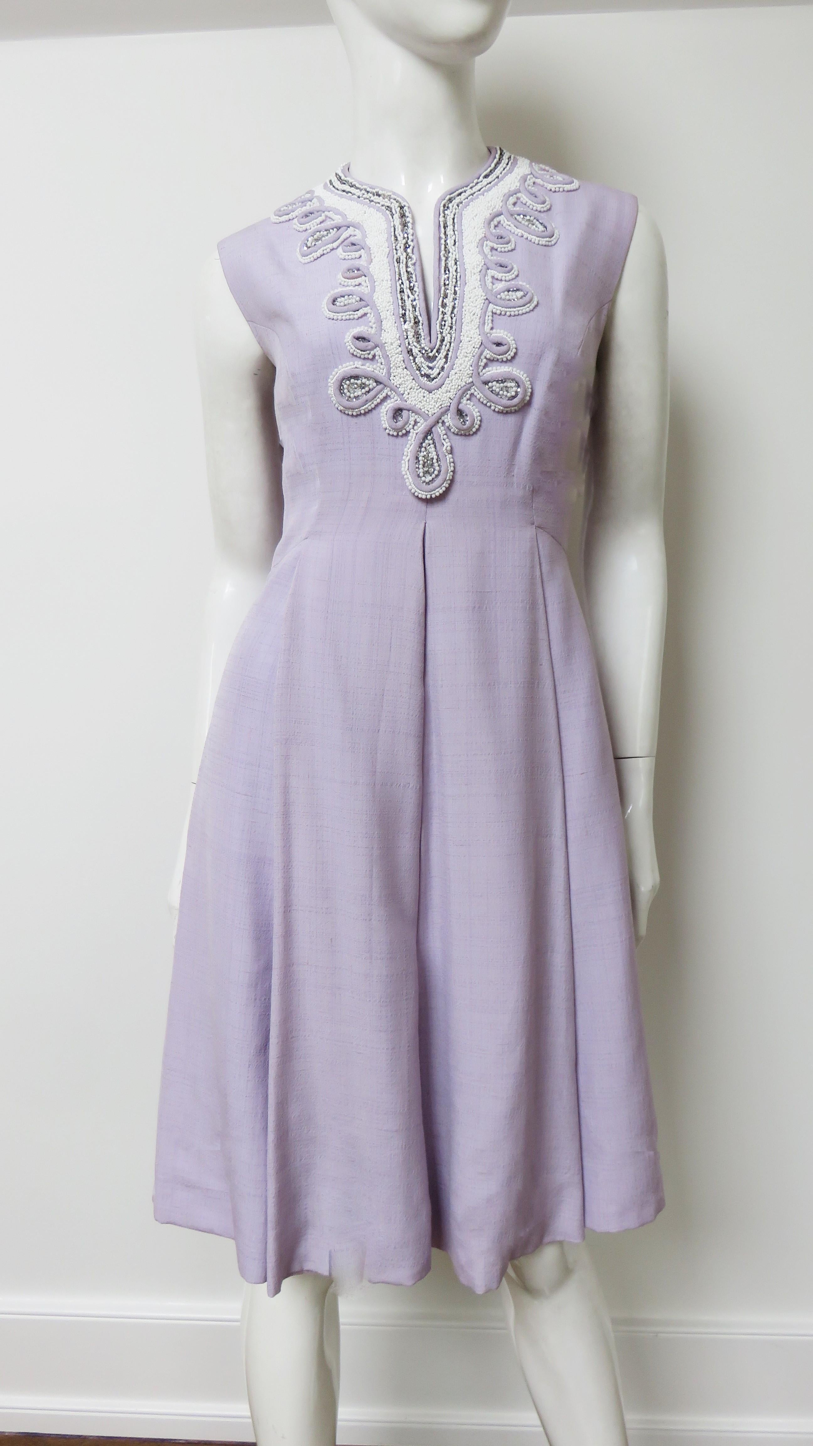 Precioso vestido de seda color lavanda confeccionado en la Hon Kong británica de los años sesenta.  No tiene mangas y presenta un escote en V con elaborados detalles de ribetes realzados con hileras de cuentas de cristal blancas. Está totalmente