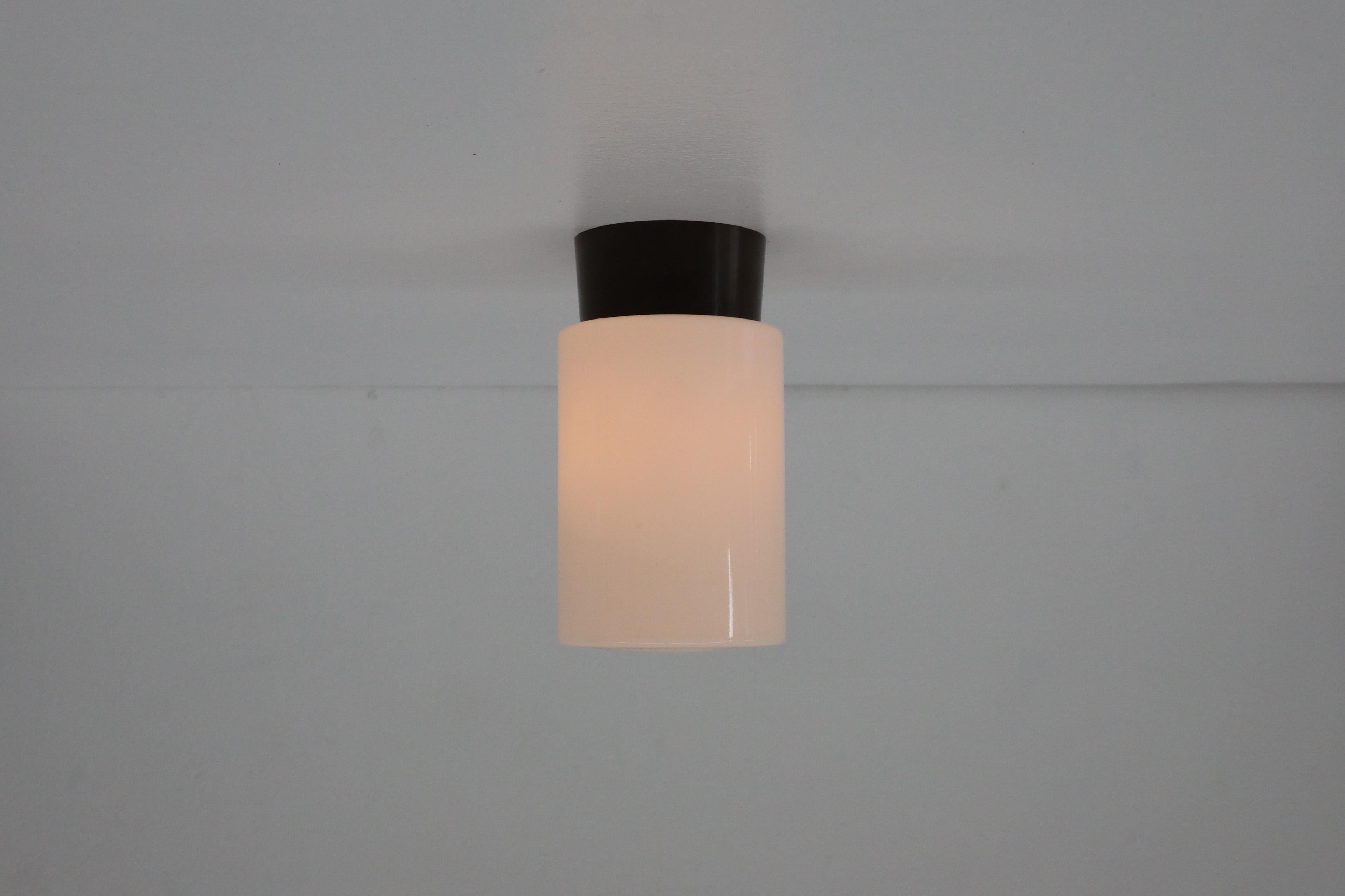 Cette applique épurée et élégante de style BEGA est dotée d'un abat-jour en verre opalin tubulaire blanc sur une monture en bakélite marron foncé. Peut être utilisée comme applique au plafond ou au mur. En état d'origine avec une usure appropriée à