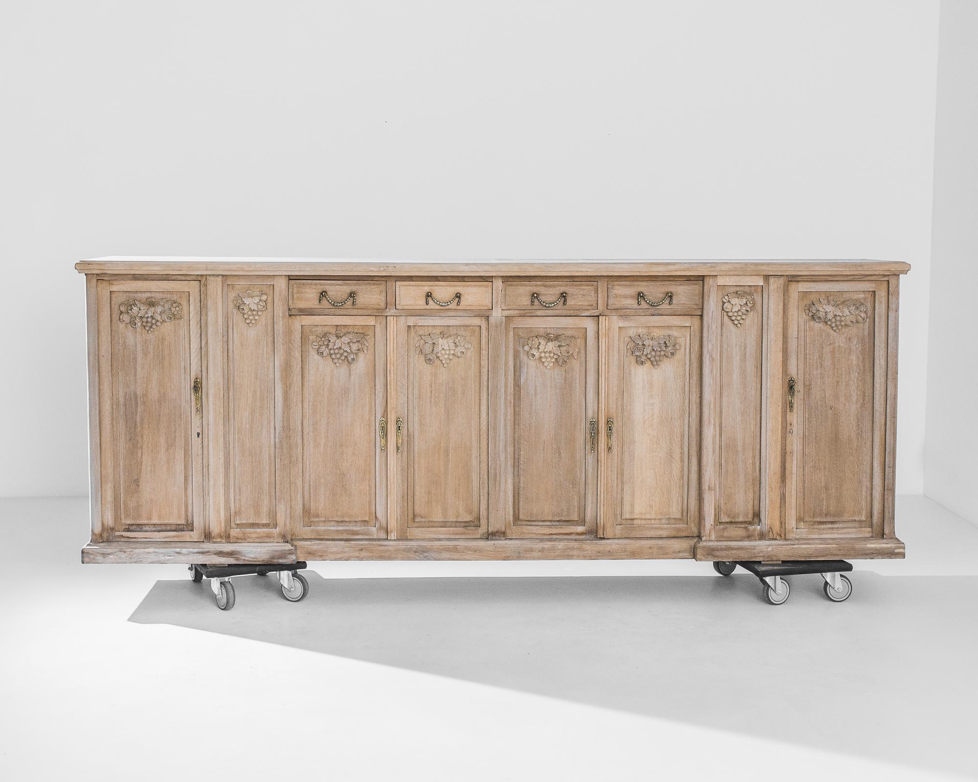 An oak cabinet from 1960s Belgium, embellished with nature morte style carvings. Each of the eight slender drawers is crowned by a carved motif of grapes, vine leaves, blowzy roses and ripe fruit: a toast to late summer abundance. The wood has been
