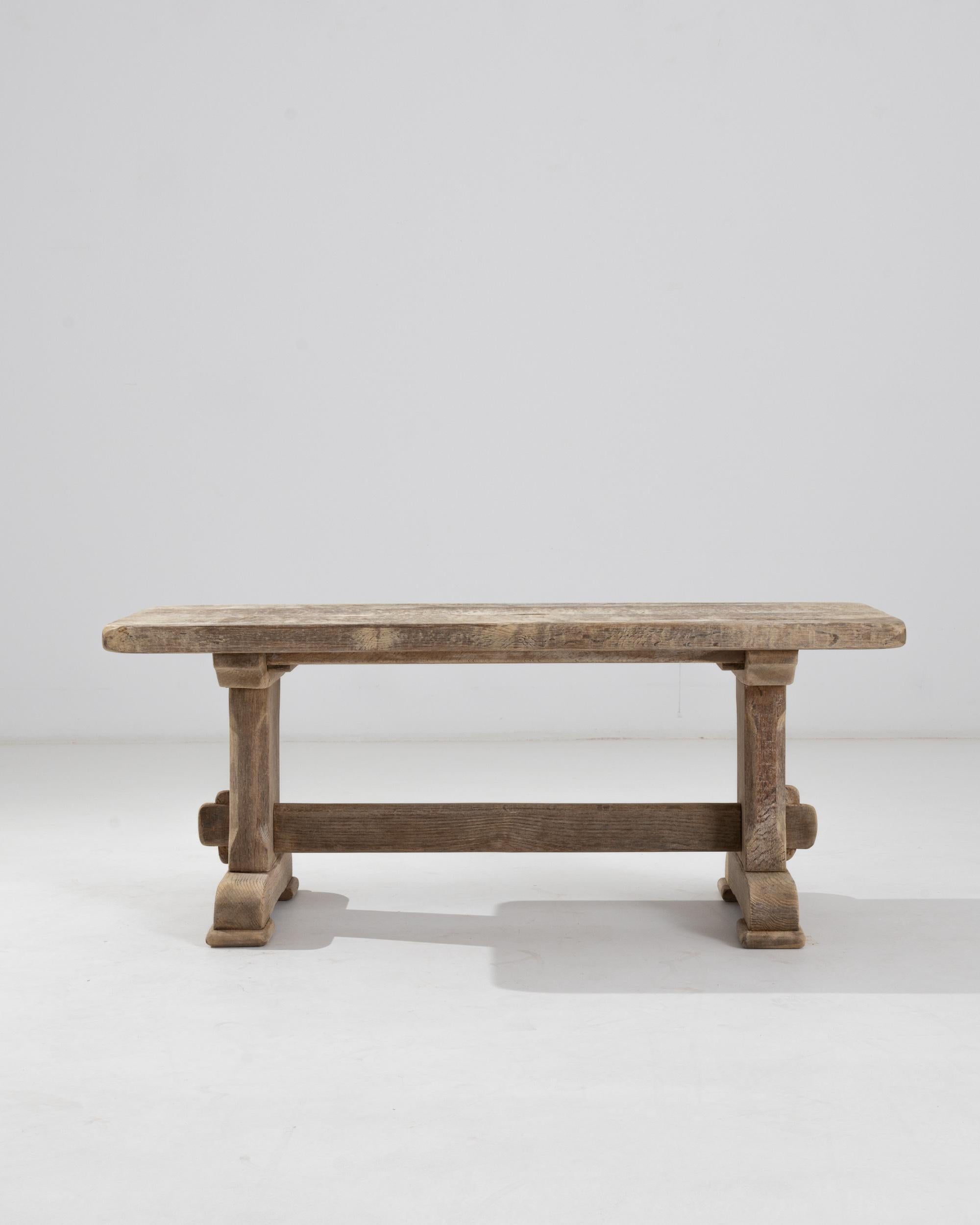 A 20th century coffee table made in Belgium. A simple wooden tabletop is raised on a carved trestle base with bracket feet that exude a solid rustic feel accentuated by the pale hue of the bleach oak finish.