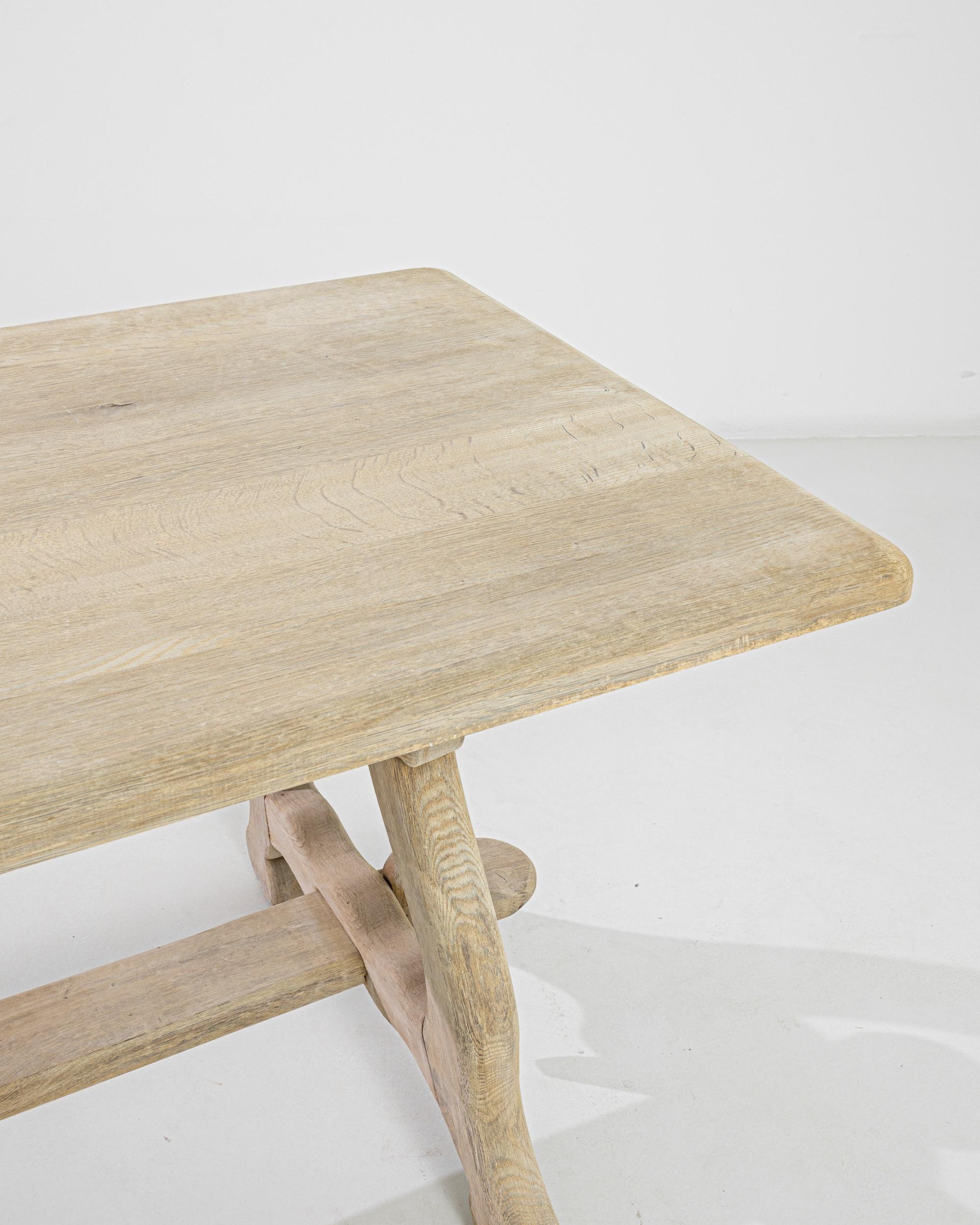 This bleached oak dining table was produced in Belgium, circa 1960. A wide rectangular top stands on sturdy carved feet, joined by a wedged middle stretcher with a mortise and tenon joint. Restored to a natural pale finish, the oak reveals organic