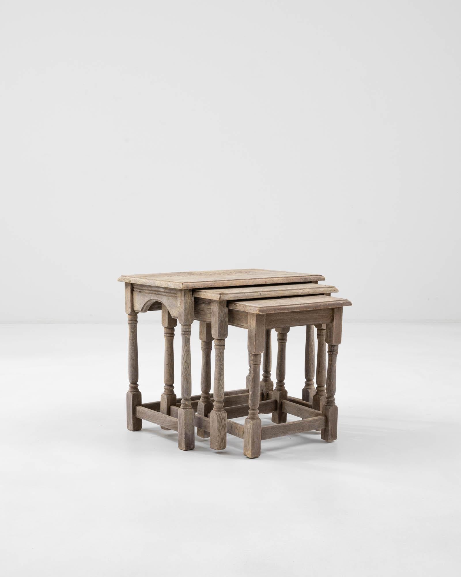 Crafted in Belgium, this vintage nesting table presents a cozy set of three. The tables, with baluster legs, mirror each other in an intriguing Escherian manner when they are put together. The bleached oak finish gives a rustic touch, endowing this