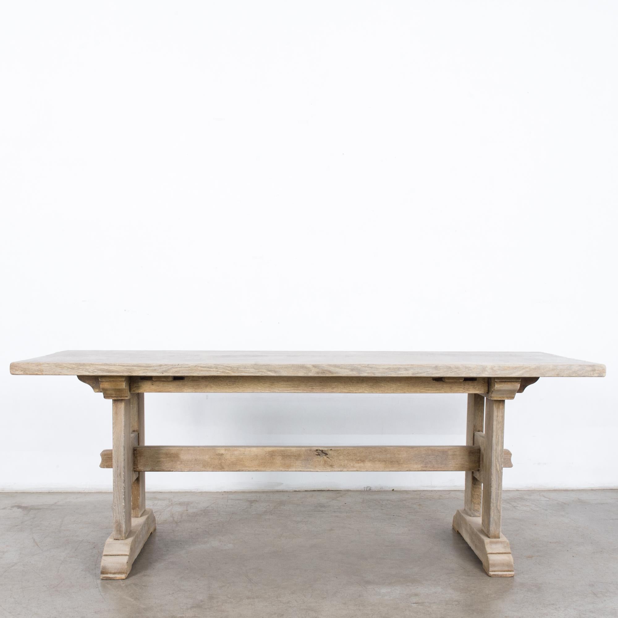 A bleached oak dining table from France, circa 1960. A sturdy tabletop sits atop trestle legs. An intricate arrangement of pegs and slats provides decorative support. The oak has been restored to a bright bleached finish. An elegant construction
