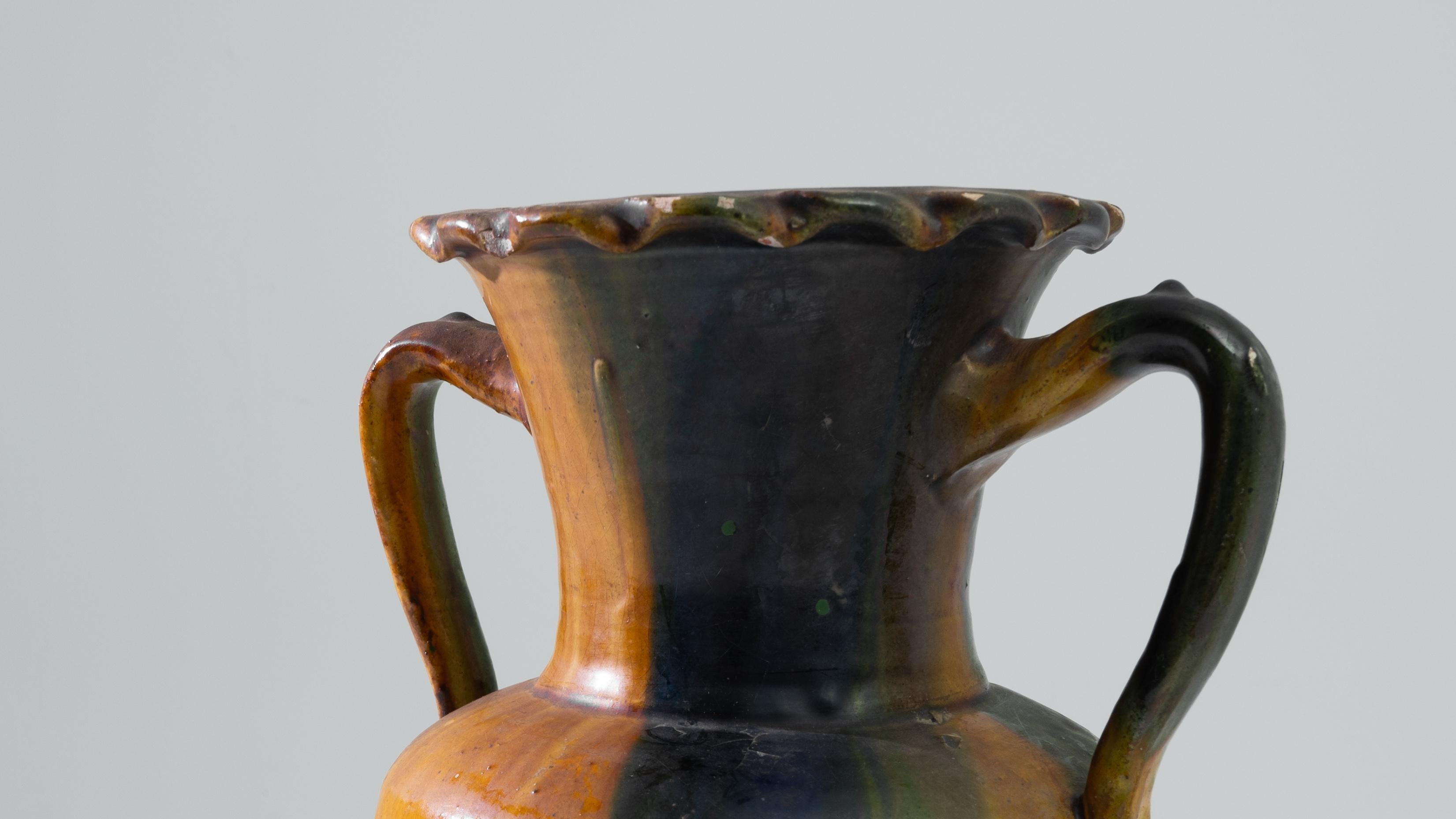 Der Charme dieser belgischen Keramikvase aus den 1960er Jahren ist ein wahres Zeugnis künstlerischen Überschwangs. Ein Kaleidoskop von Farben - Orange, Blau und Grün - plätschert in einem lebhaften Tanz der Farbtöne über seine Oberfläche. Die Vase