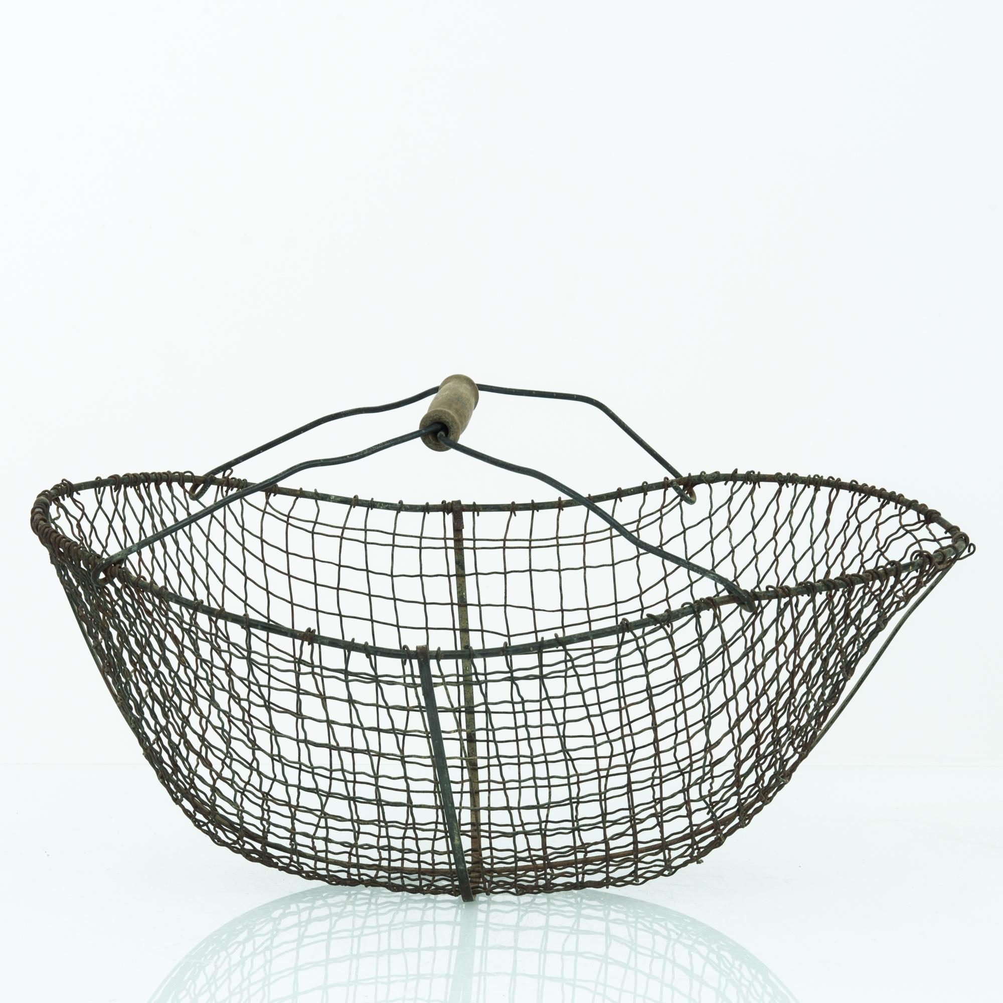This basket was made in Belgium, circa 1960. Woven from thin metal wires, the basket displays a netted, organic structure with depth and a gentle flare. With a storied patina, this time-worn basket makes a charming cradle for future collections. A