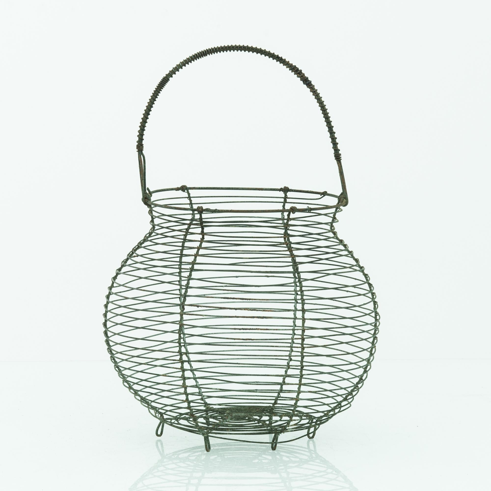 This basket was made in Belgium, circa 1960. Woven from thin metal wires, the basket displays a netted, organic structure with depth and a gentle flare. Resting on tiny feet, the pot shape is accentuated with a heavy wire handle.