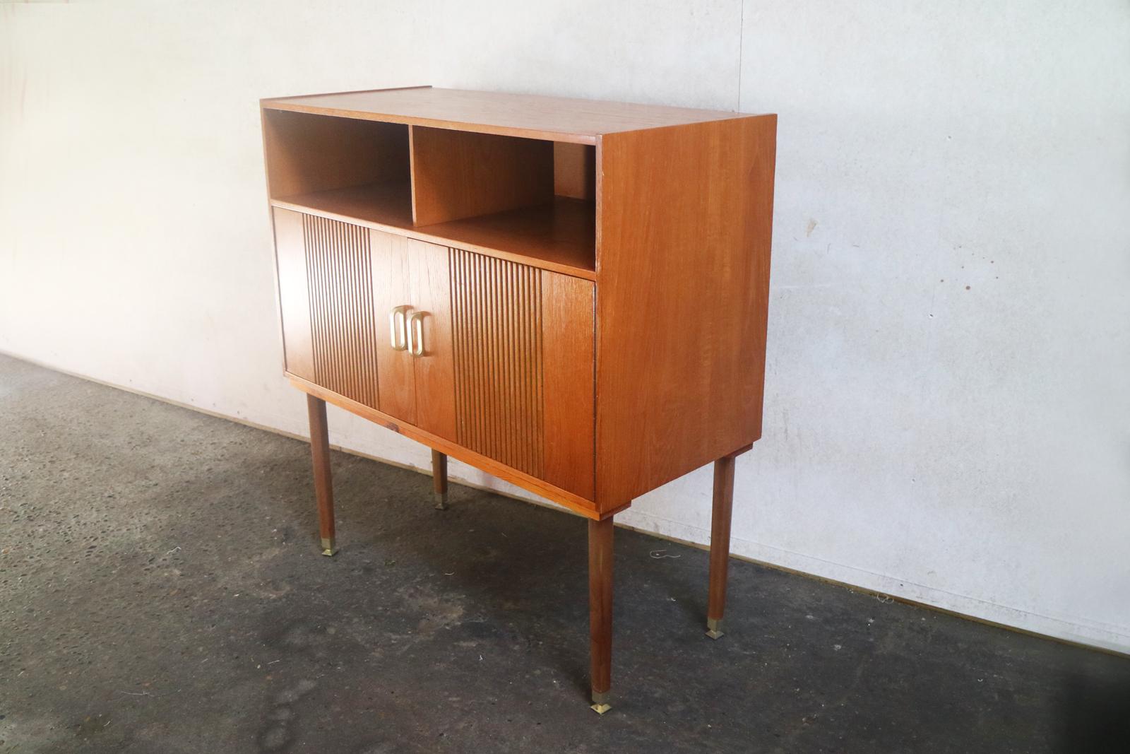 A neat Mid-Century Modern sideboard made in Belgium in the 1960s. Two open alcoves sit above a two door cupboard. Ridged detail and stylish brass handles. Sits on elegant thin feet with brass tips.

Country of origin: UK
Date of manufacture: