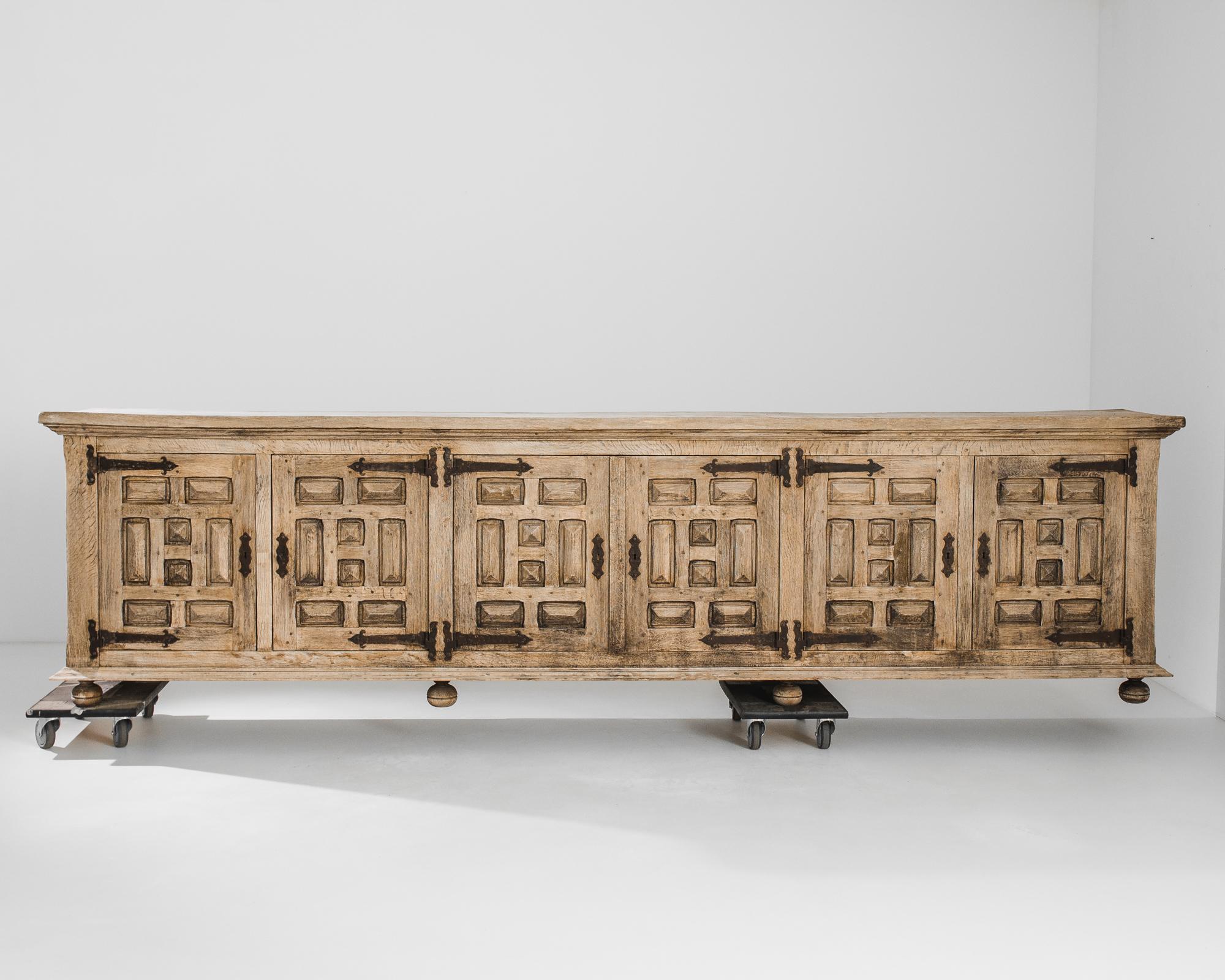 An electric mix of styles give this oak buffet a unique appeal. Made in Belgium in the 1960s, the long case is elevated upon ball feet; graphic diamond-point moldings decorate the cupboard doors. Iron door hinges and lock pieces, weathered to an