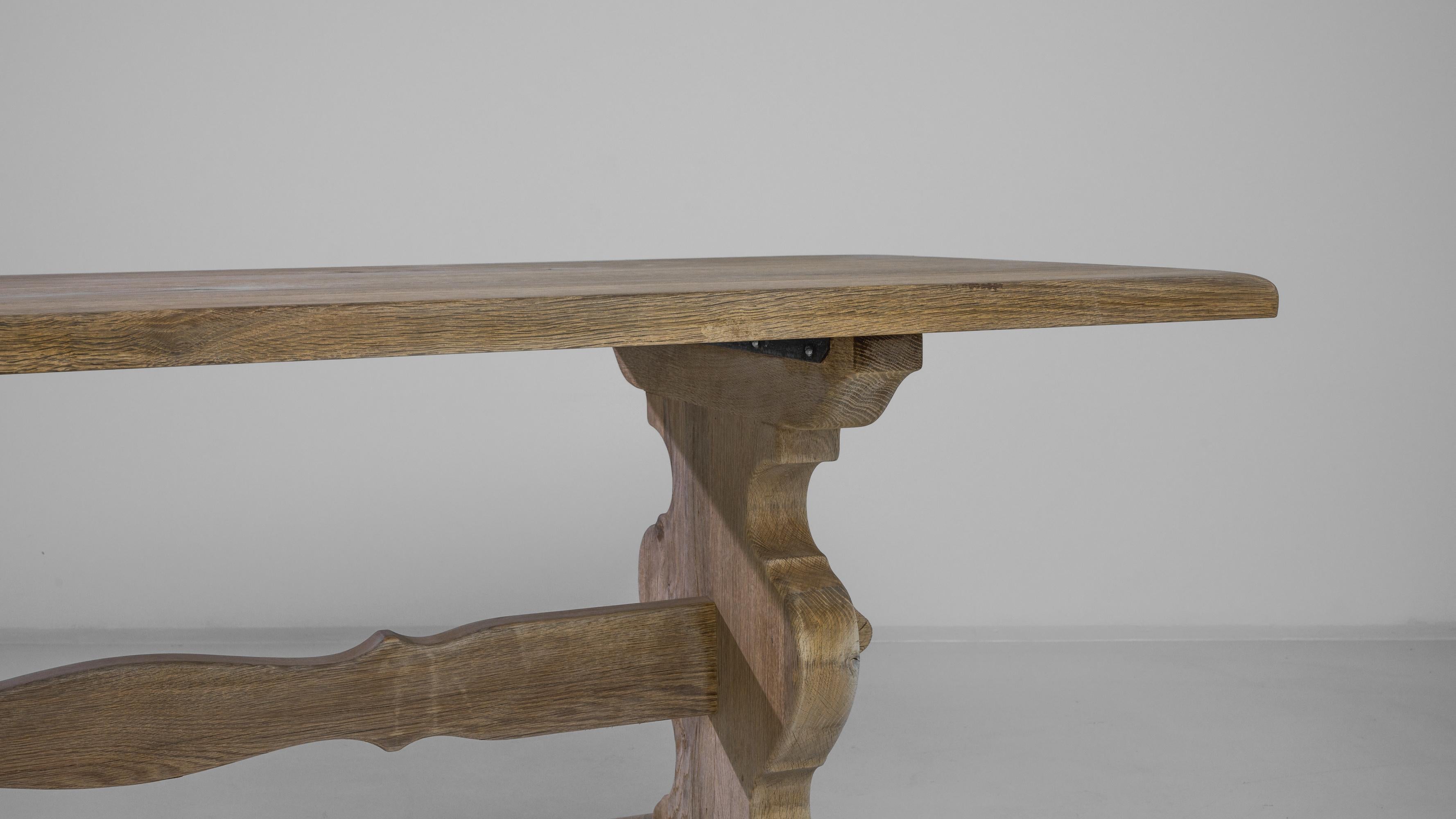 This bleached oak dining table was produced in Belgium, circa 1960. A wide rectangular top stands on sturdy carved feet, joined with wooden pins to a center stretcher. Restored to a natural pale finish, the oak reveals a variation in tones,