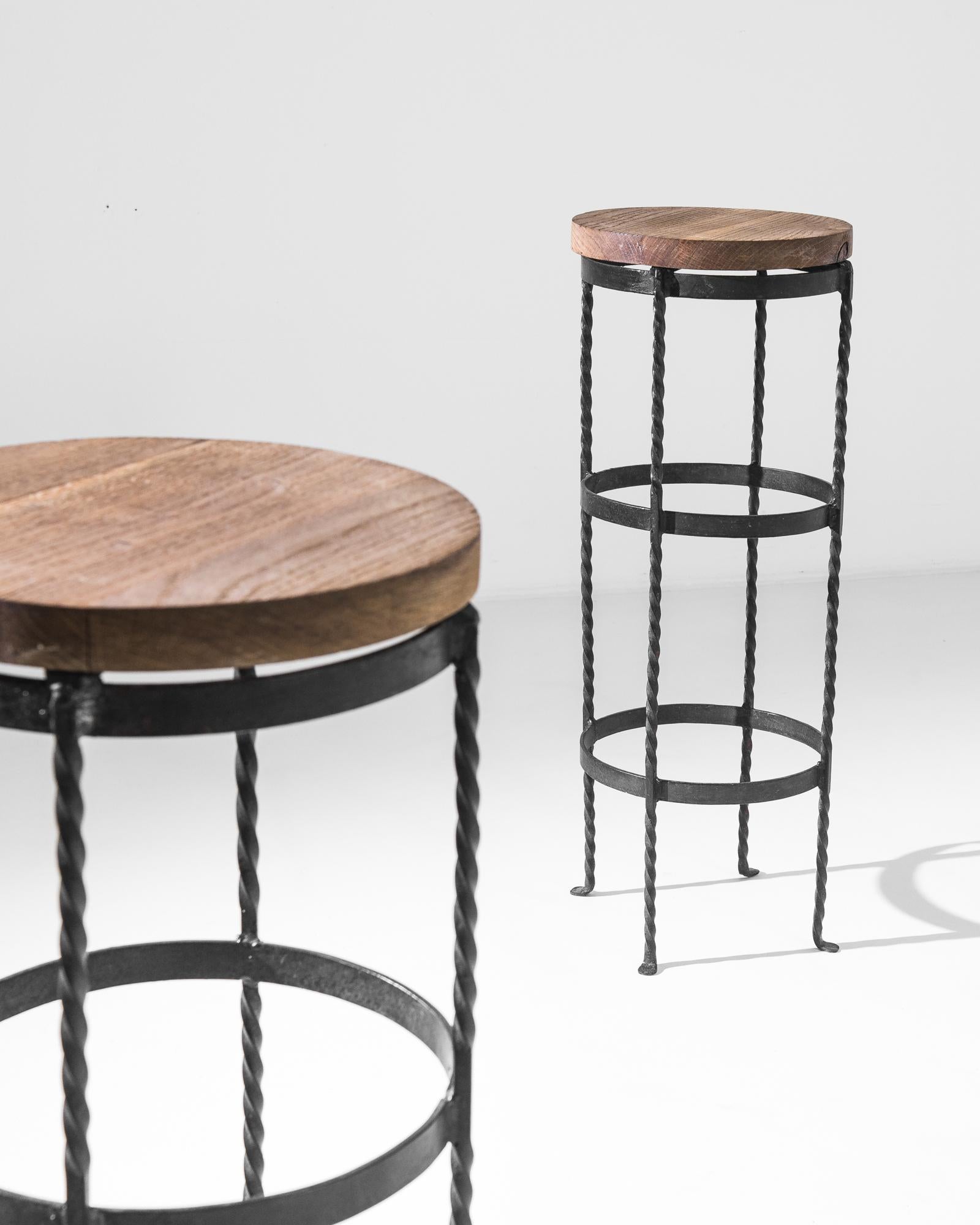 This pair of vintage metal stools was produced in Belgium, circa 1960. A thick cut of wood lays upon high twirled legs, belted by three metal rings. The association of the wrought iron and the natural wood offers a pleasing contrast of materials and