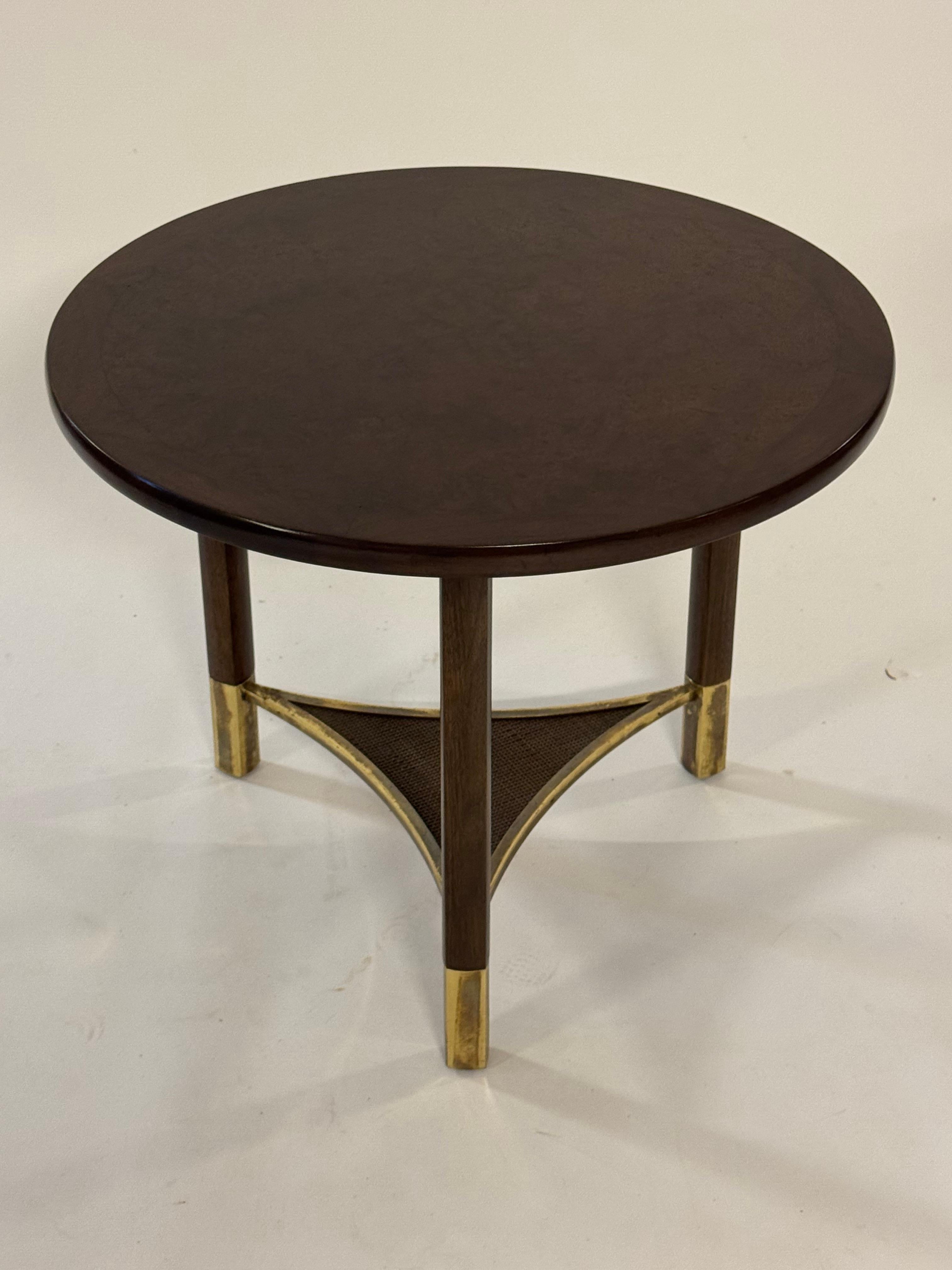 La rivisitazione in chiave Mid-Century Modern degli anni '60 di una forma classica realizzata da Bert England per Johnson Furniture Co. Questo tavolino rotondo a tre gambe ha un piano in legno burattato con bordo a fascia, una struttura in mogano