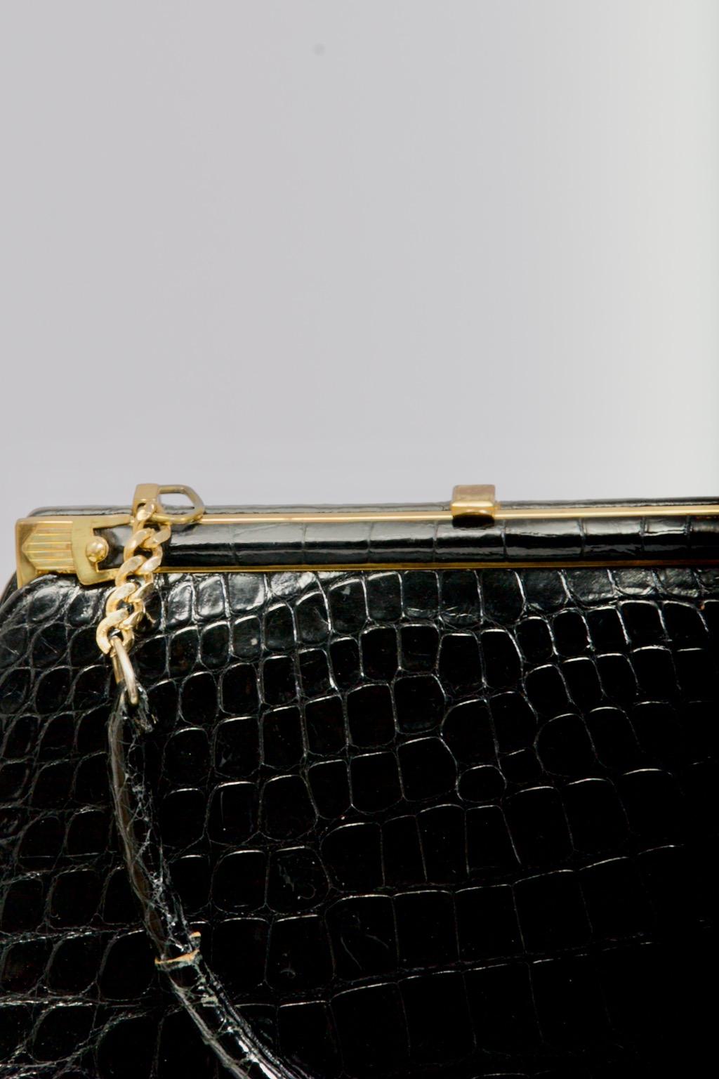Classic vintage black alligator handbag features gold tone hardware and a single handle attached to the frame with a 5-link chain on each end. The interior is black leather with side compartments and fabric tag marked 
