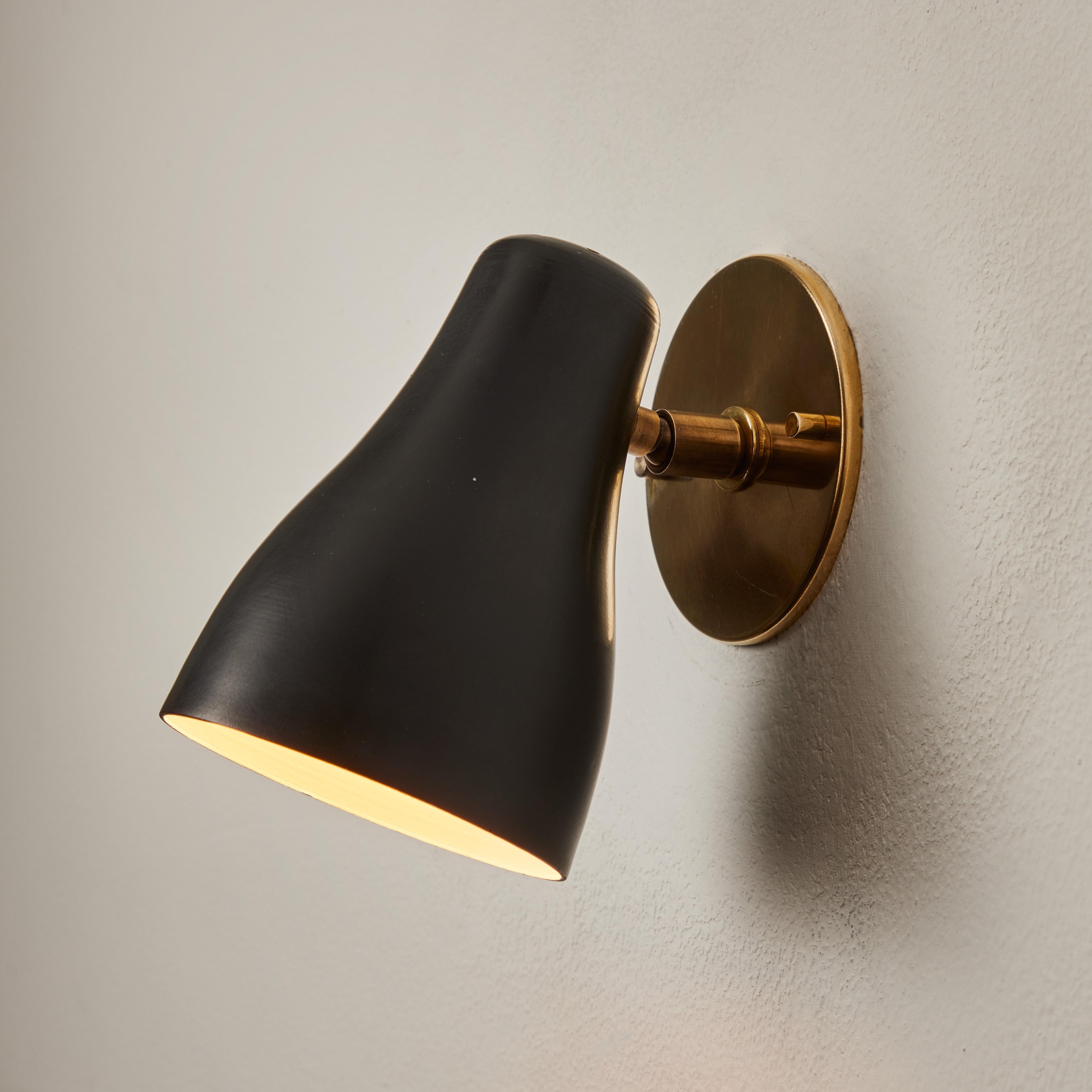 1960s Black and brass wall lamp attributed to Jacques Biny. An exceptionally clean and simple design executed in brass with a black metal shade. Lamp rotates freely on adjustable swivel. Quintessentially midcentury French in its conception and