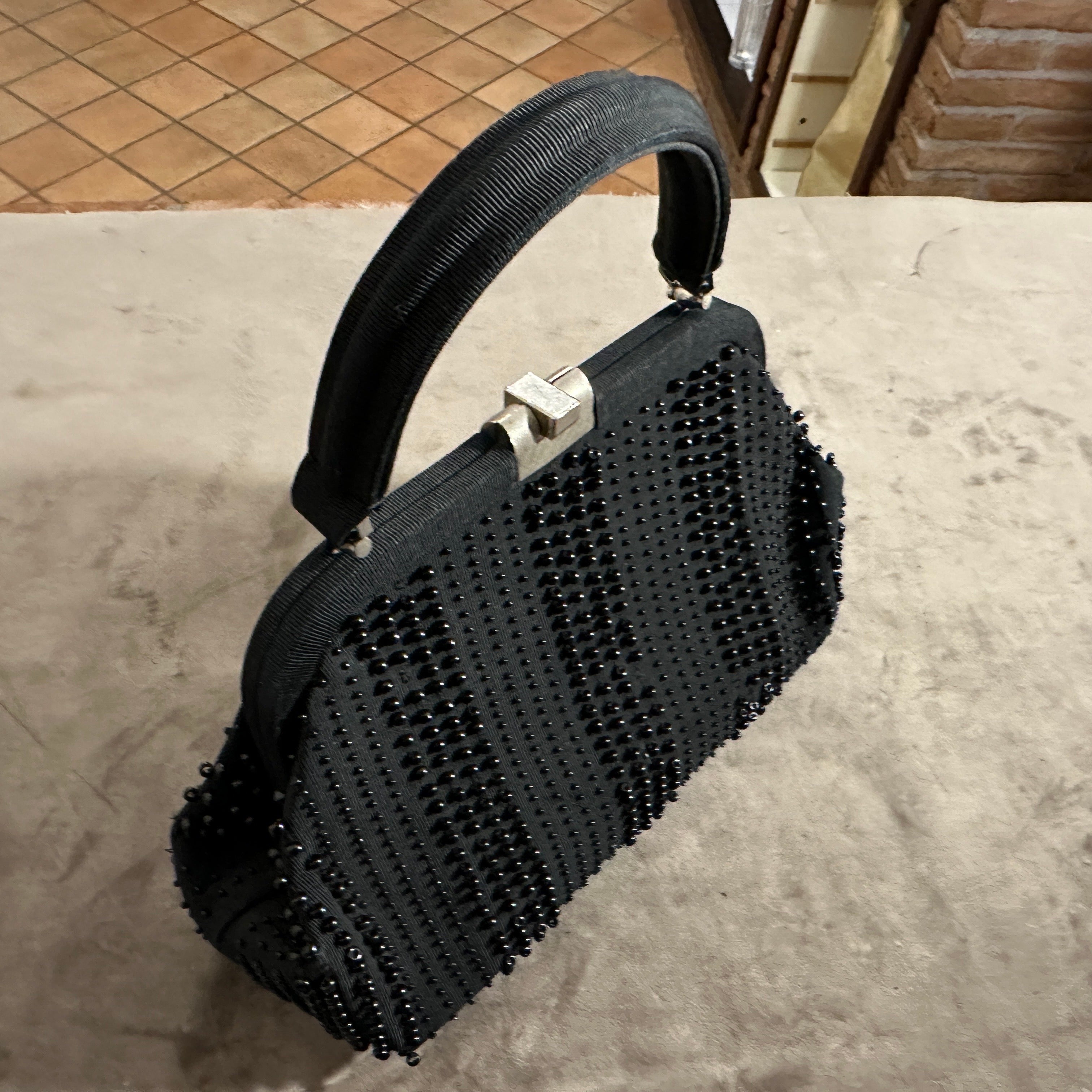 Vintage 1960s Italian Black Beaded Evening Bag
This stunning vintage black evening bag is an exquisite example of Italian design from the 1960s. This piece is a beautiful blend of texture and sparkle, perfect for adding a touch of classic glamour to