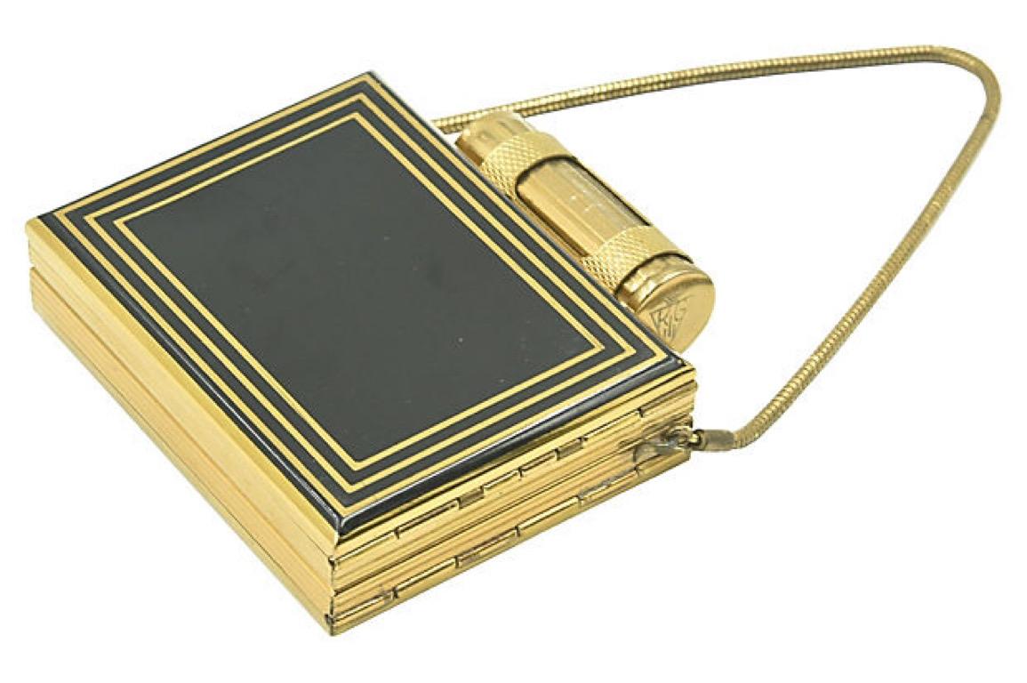 1960s Kigu goldtone metal compact/cigarette case with a rounded clasp on top for holding lipstick. Features a Deco-style design in black and 7