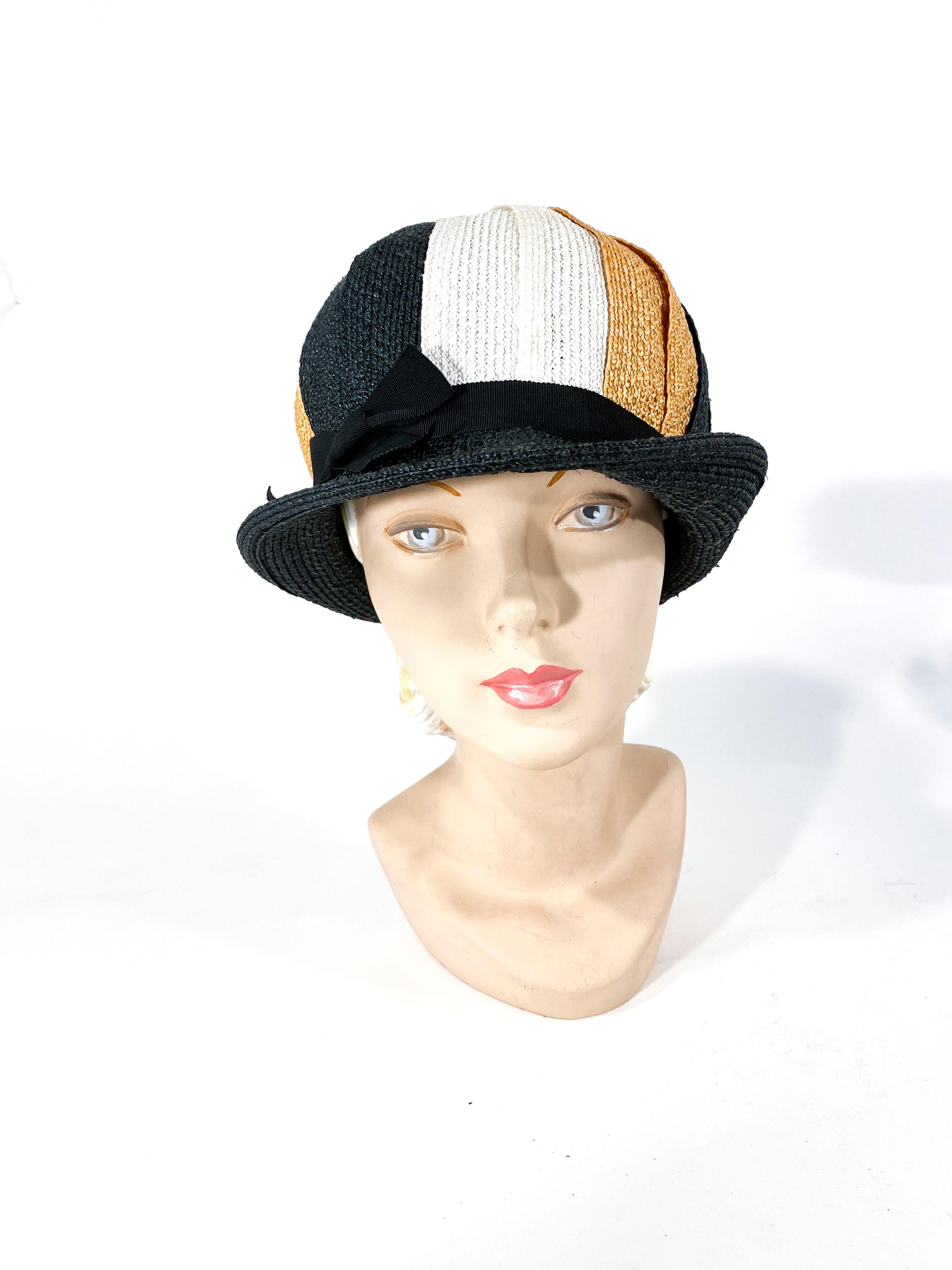 1960s woven raffia hat in black, gold, and cream in a pinwheel pattern. It has a very mod 