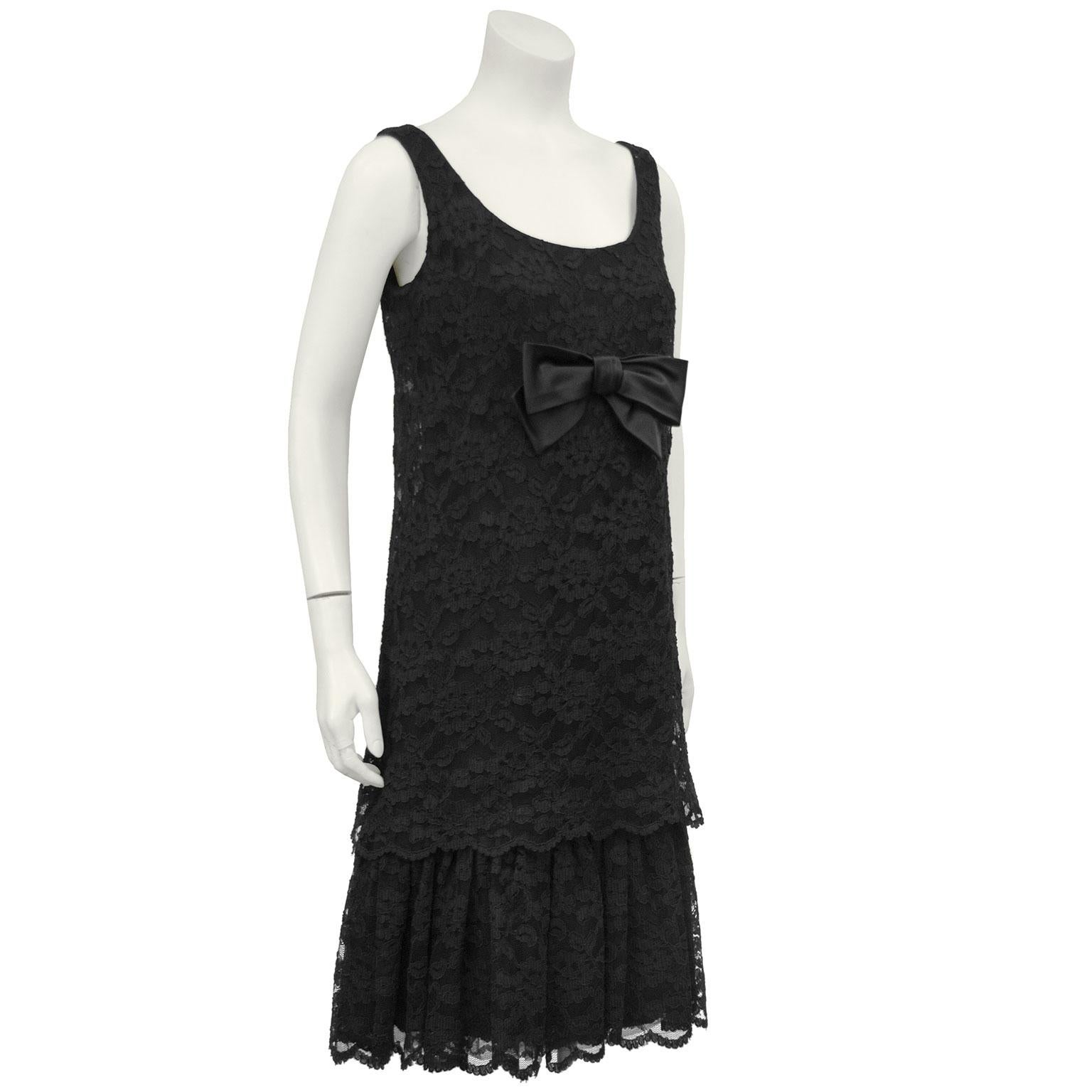 Black 1960s lace drop waist cocktail dress with the label Anita Modes. The sleeveless dress has a full black lace overlay with an added hem detail. Large black taffeta bow at the bust. Inner dress zips up the back, lace layer closes with snaps. In