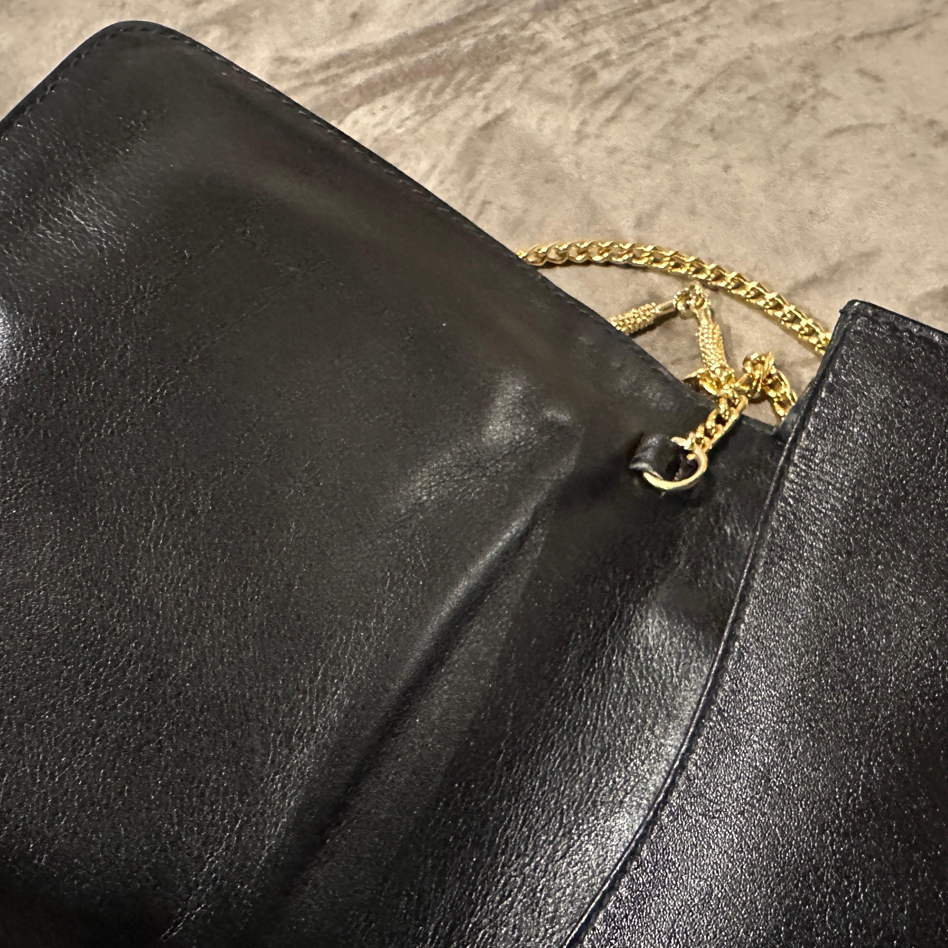Cette pièce élégante associe des matériaux classiques à un design épuré et minimaliste, ce qui en fait un accessoire intemporel pour toute occasion formelle.
Le sac est doté d'un boîtier rigide distinctif en bakélite noire brillante, qui lui confère