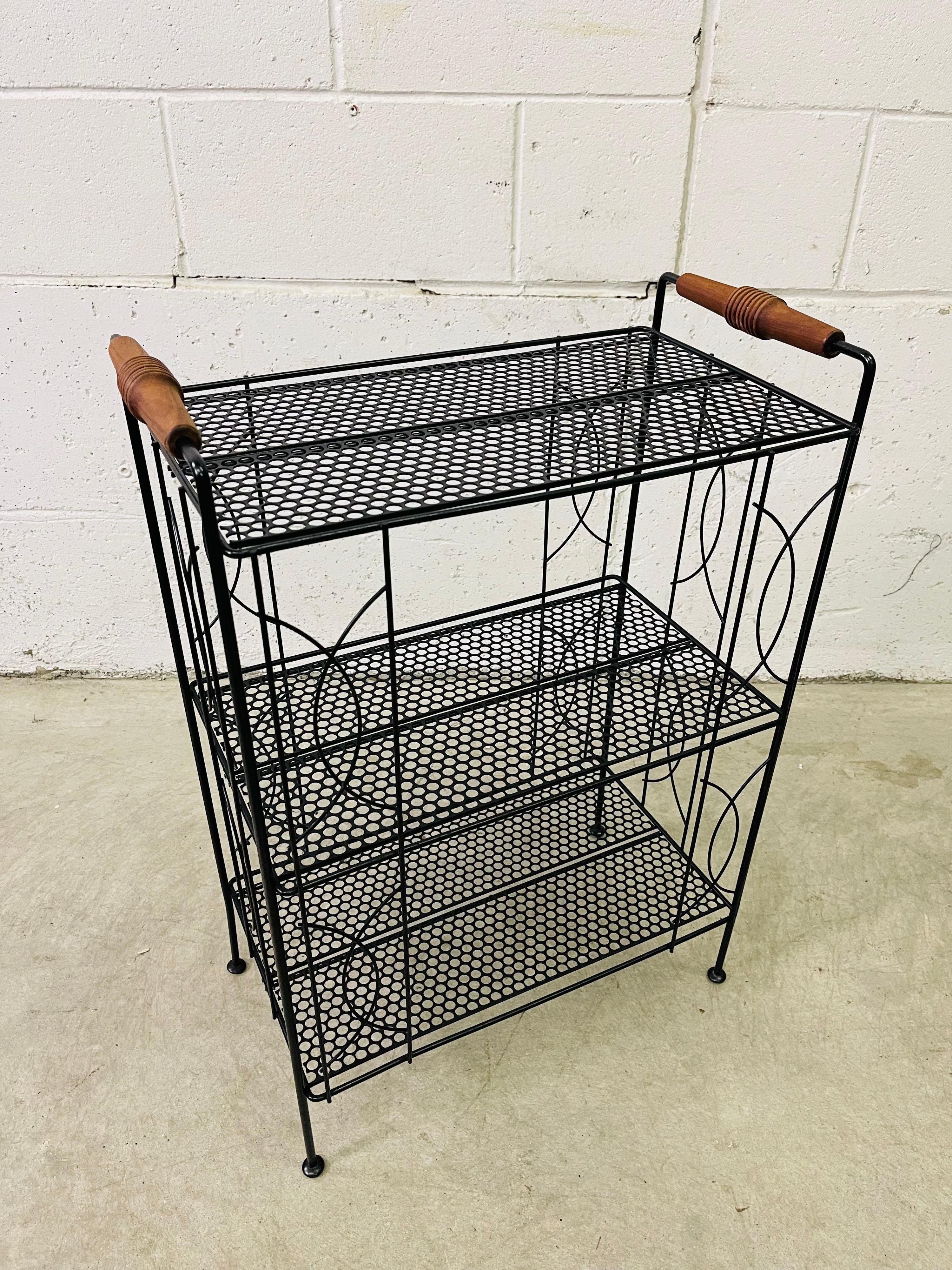 Vintage 1960s black metal storage shelf with walnut wood handles. The stand has three shelves for storage and nice decorative accents on the back and sides. No marks.