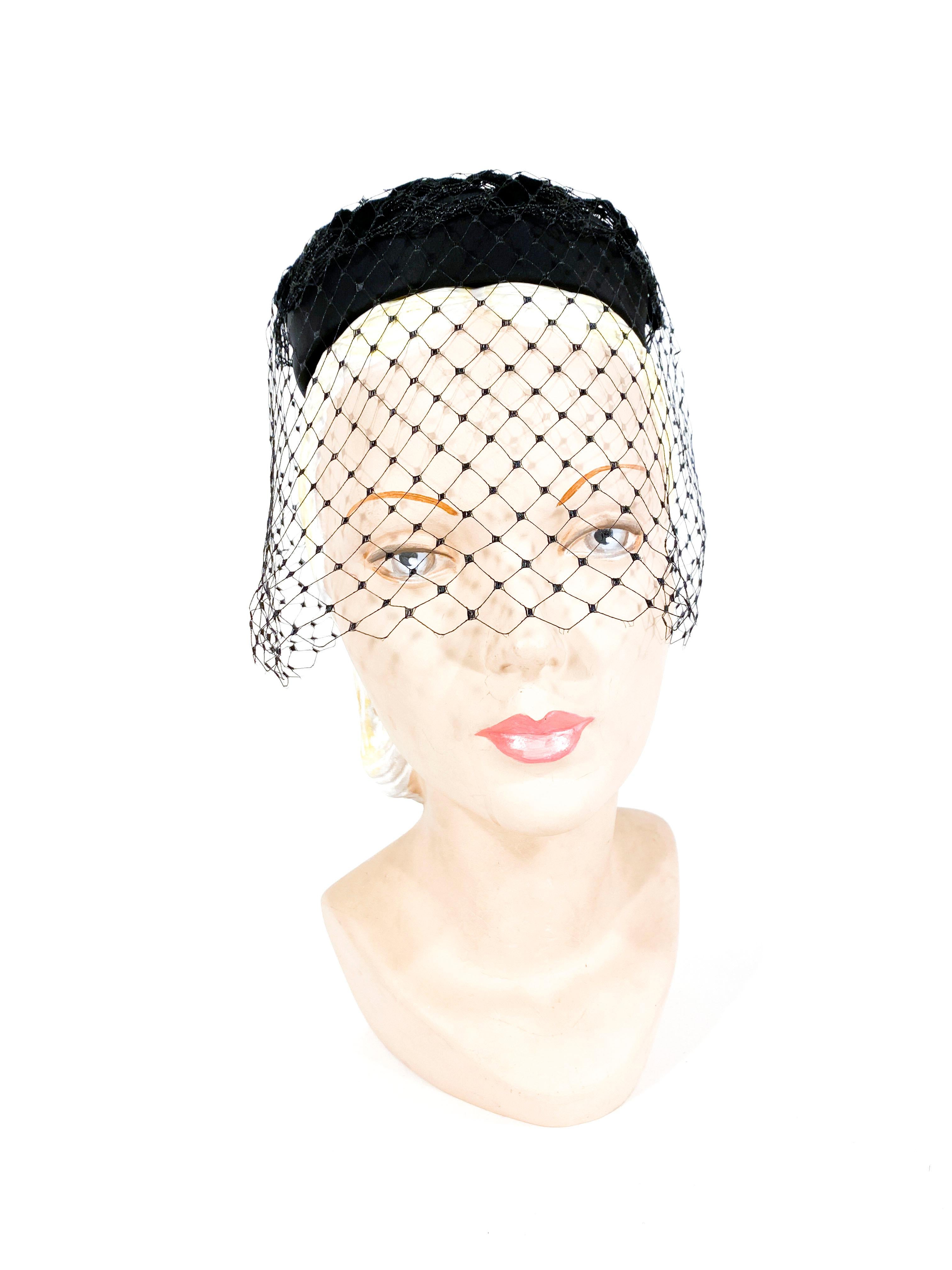 1960s black satin pillbox hat with a zig-zag velvet ribbon intertwined in the net. The net covers all around the head dropping down to past the bridge of the nose. 