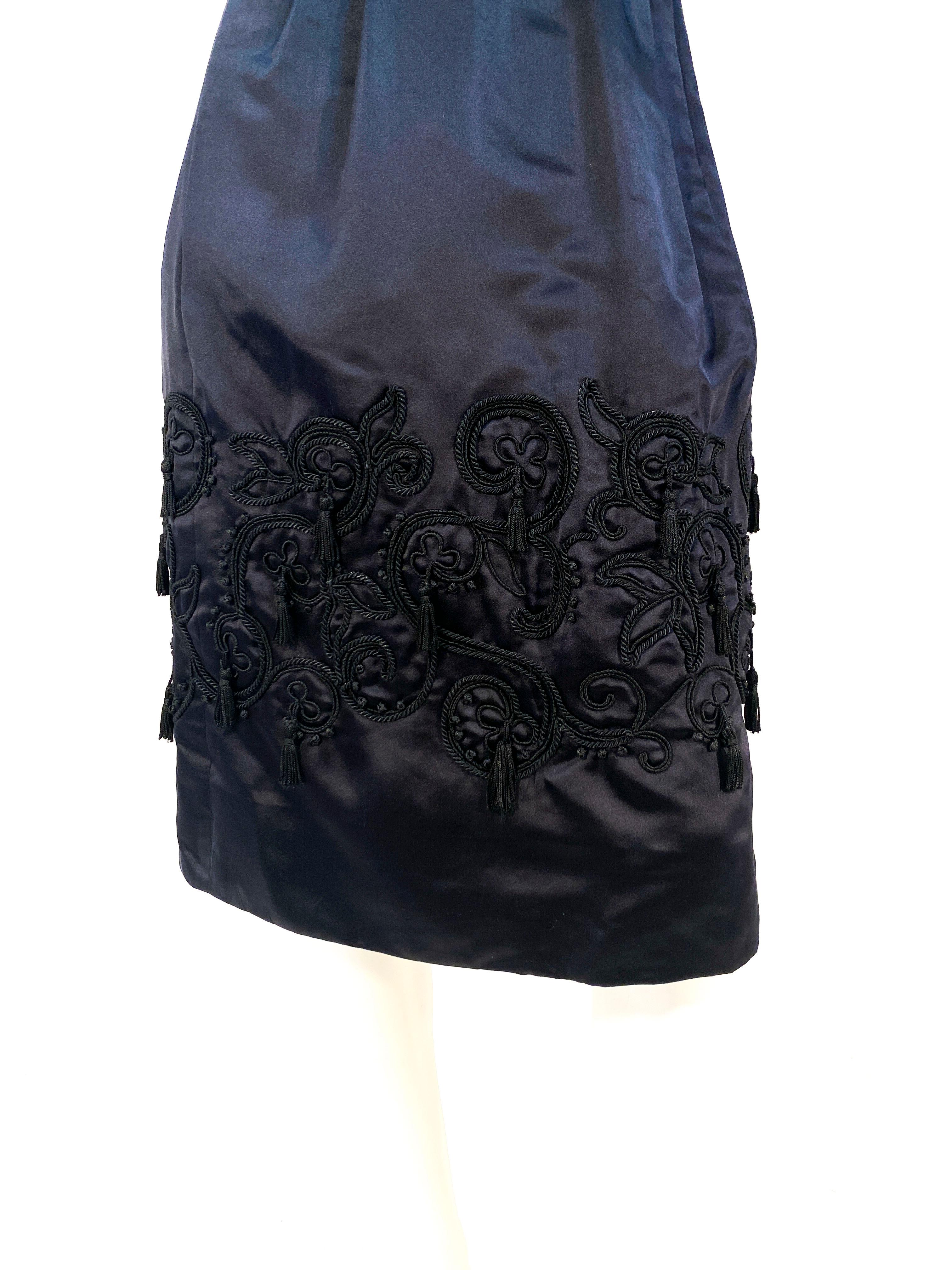 1960s custom made and handmade black silk satin cocktail dress featuring a wide boarder embroidery of soutache, french knots, and tassels located on the bottom of the skirt. The dress has a hand-set zipper back closure and a piped rope waist that
