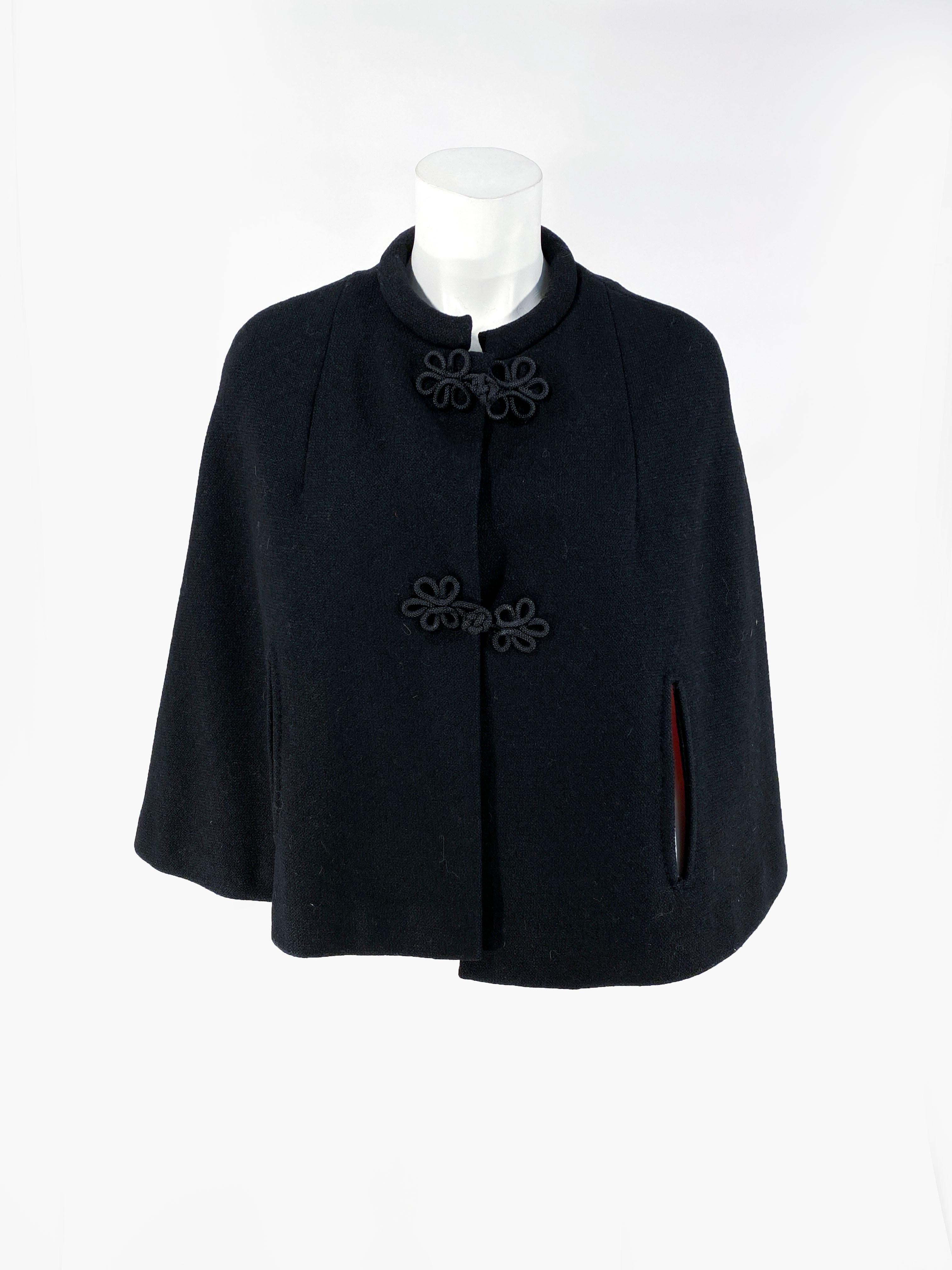 1960s black wool caplet with a vibrant red satin lining. This piece is decorated with handmade cord frogs, and handset are slits. The rolled collar is padded from a comfortable fit around the neck. The measurement across the shoulders is 17 inches.