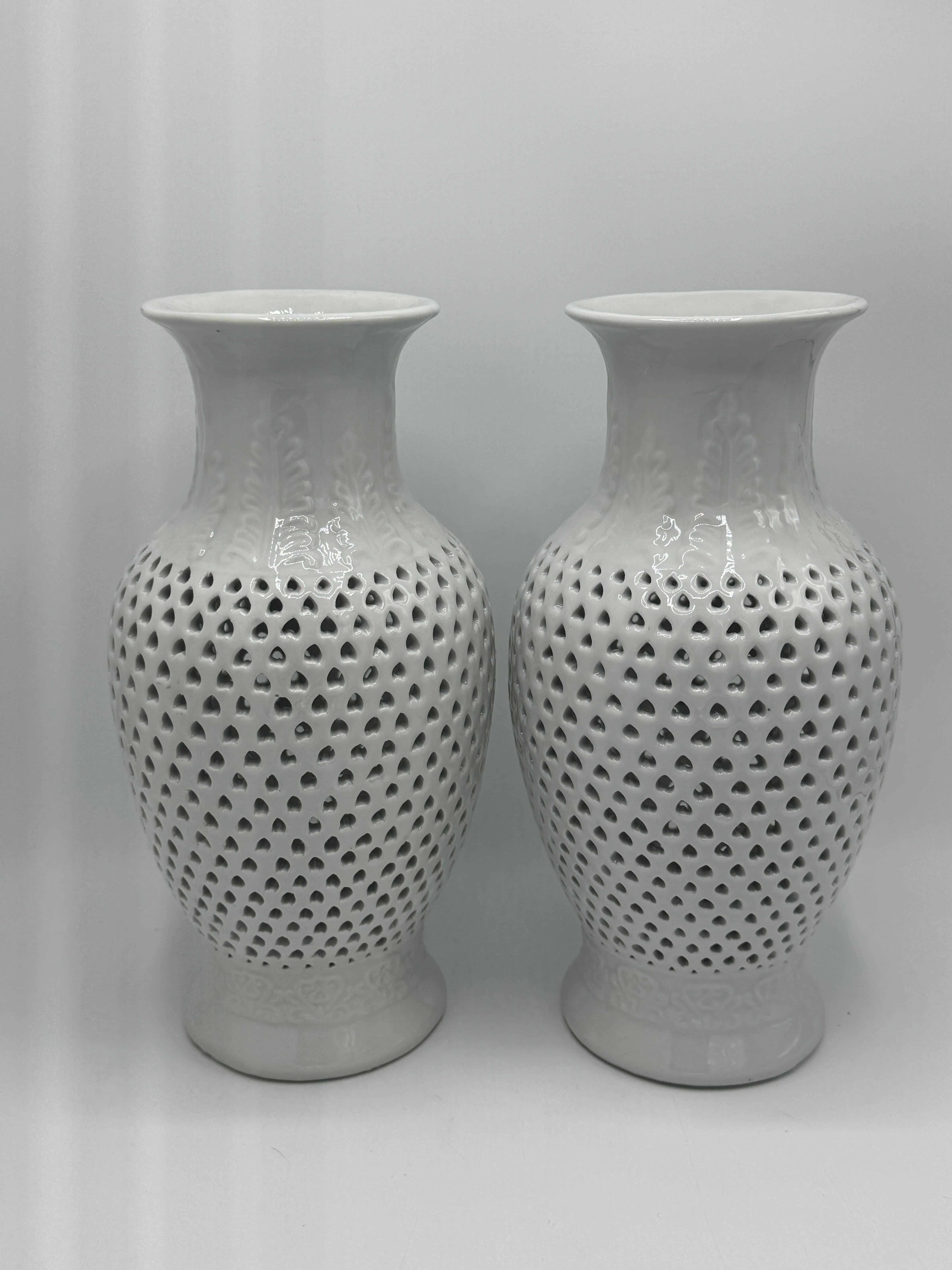 Offered is a fabulous, pair of 1960s Blanc de Chine pierced porcelain urns. The pair feature a pierced design over the center body, with a raised leaf motif along the neck and base. On the underside, there are holes large enough to have these urns