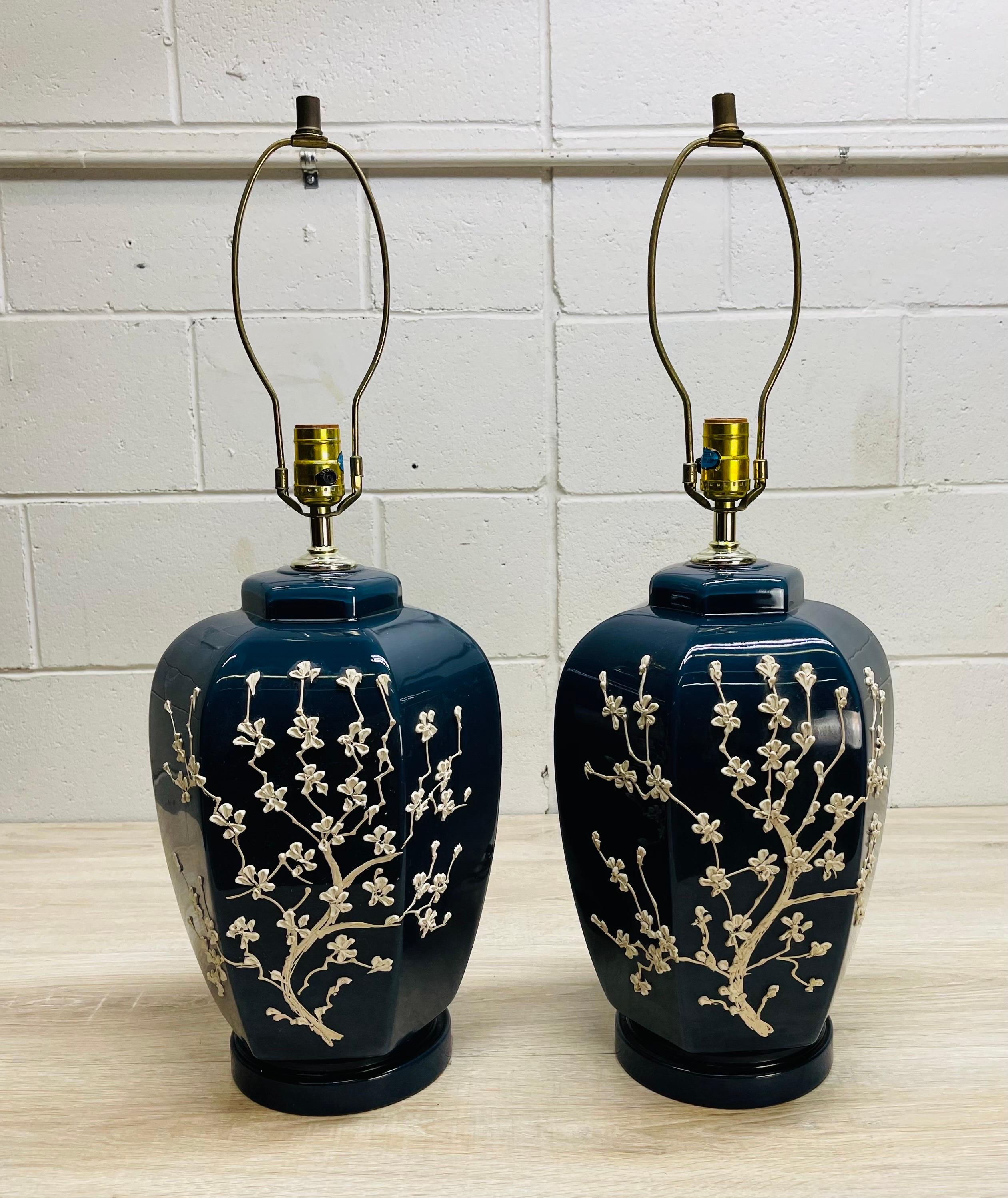Vintage 1960s pair of blue ceramic six sided table lamps with white aplied flowers. The floral design covers the front and sides of the lamps. The lamps are wired for the US and in working condition. The lamps use a standard 100W bulb. Socket, 19”H.