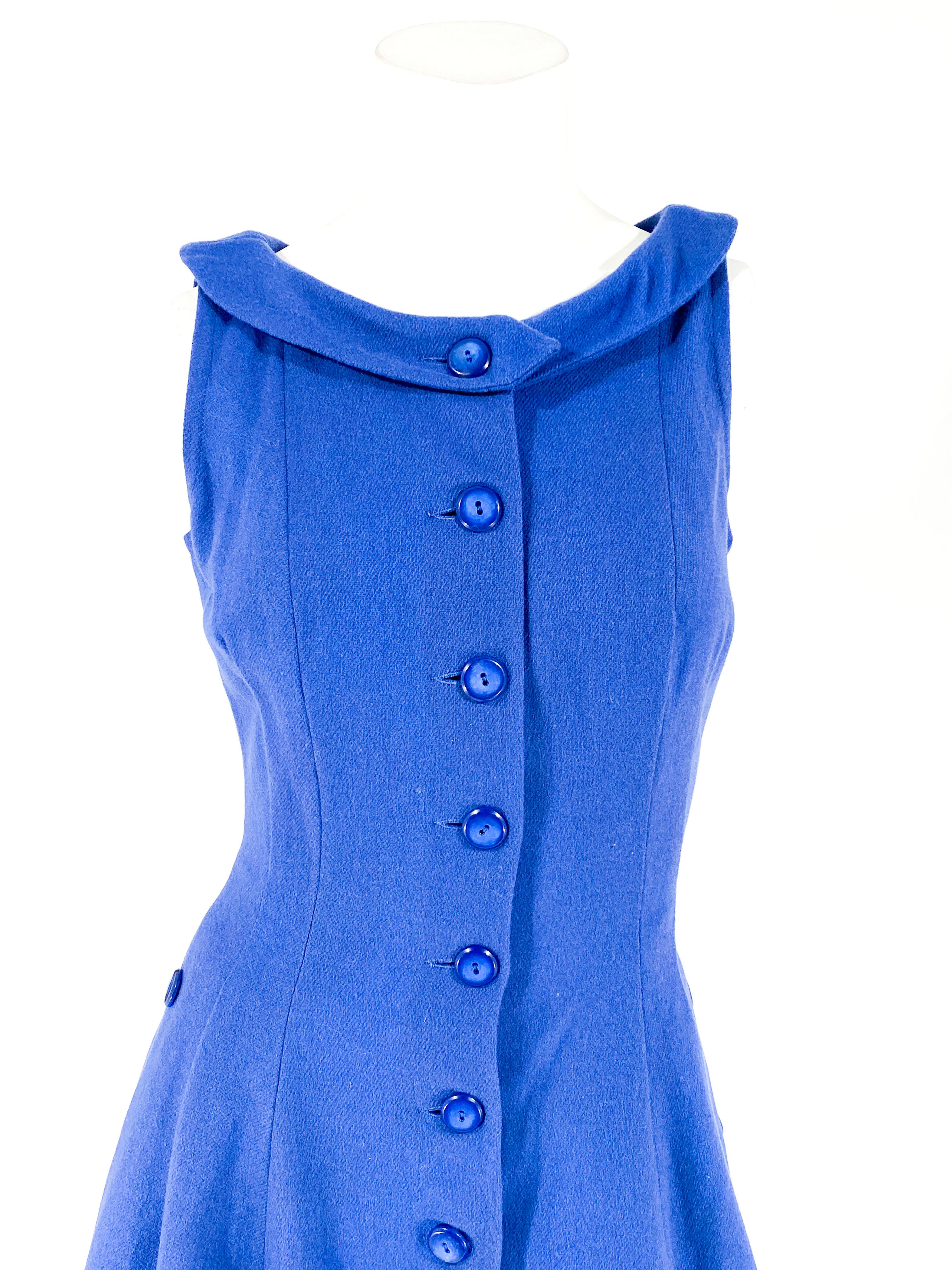 Vestido de lana azul de los años 60 ajustado a la cintura con falda acampanada. La parte delantera del vestido tiene un cierre de botones que llega hasta más allá de la cadera. Los laterales están adornados con botones adicionales que acentúan los