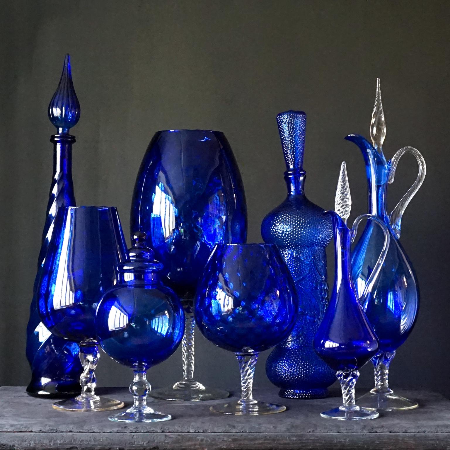 Very decorative midcentury blue set of eight different Size large Italian glass pressed genie bottles and blown clear and blue glass vases and a candy jar in different shapes in a deep shade of cobalt blue.

Produced in midcentury Empoli, Florence