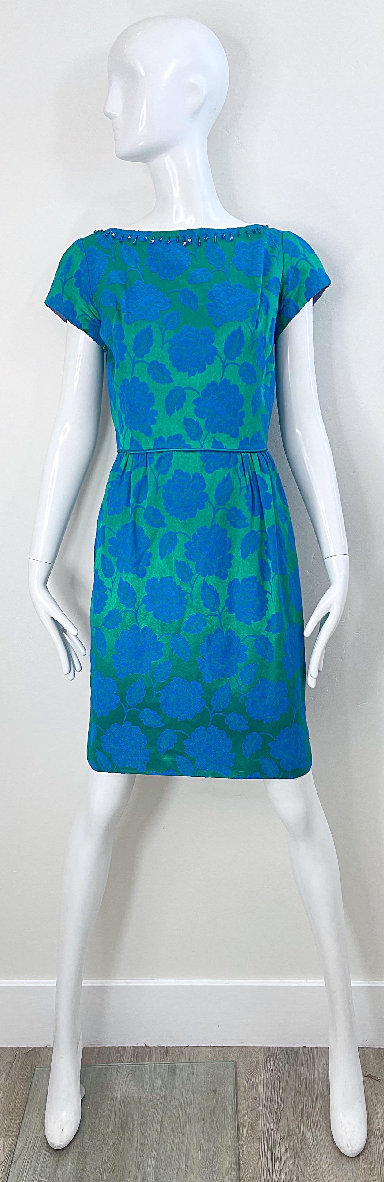 Magnifique robe fourreau du début des années 60 en soie damassée bleue et verte à imprimé floral, manches courtes et perles ! Le luxueux tissu en soie présente juste ce qu'il faut de brillance. Perles bleues autour du cou et du dos. Fermeture à