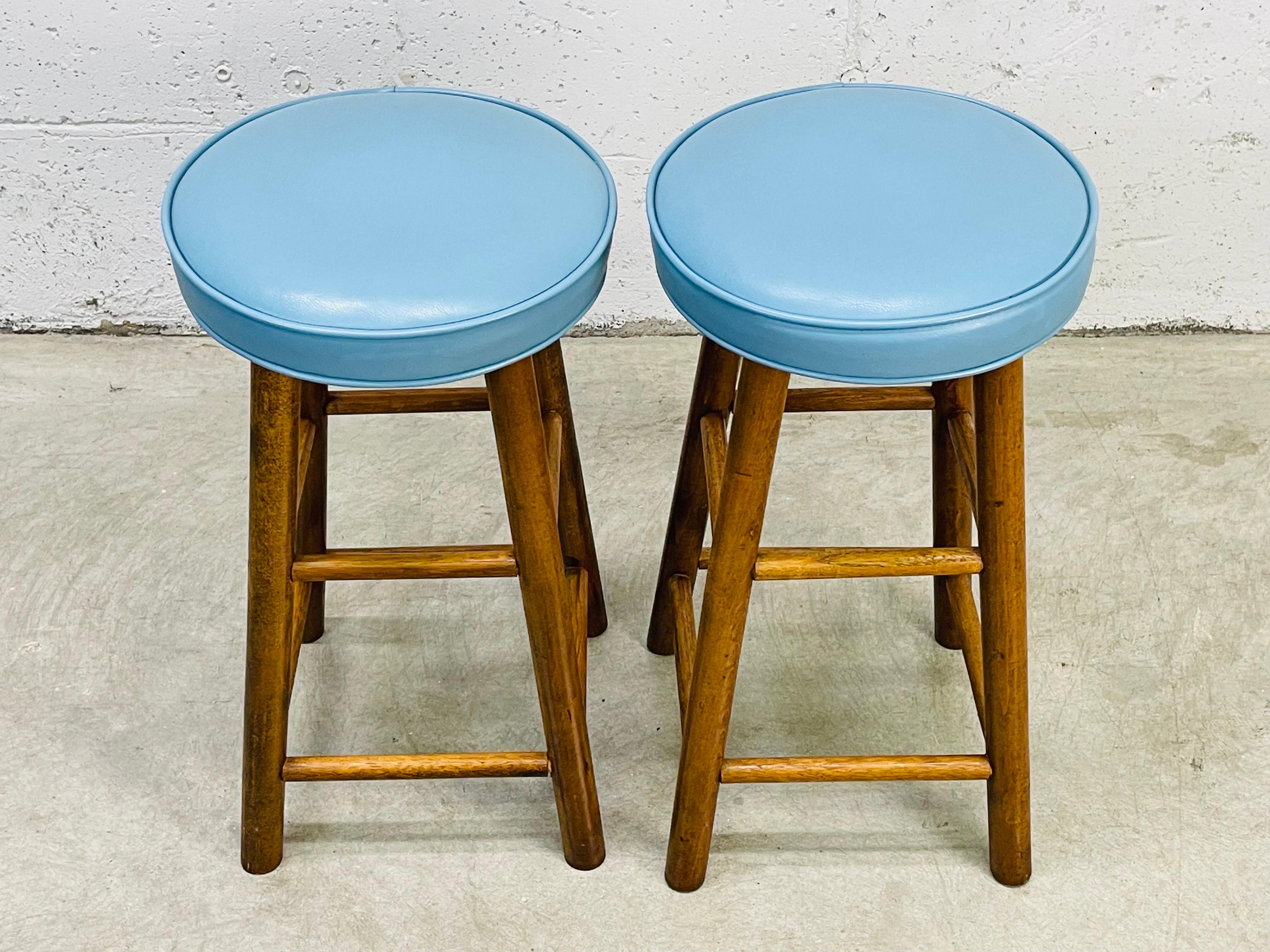 Vintage 1960s pair of blue round vinyl top low bar stools with a maple wood base. Vinyl is in excellent condition and the stools are both sturdy. No marks.
