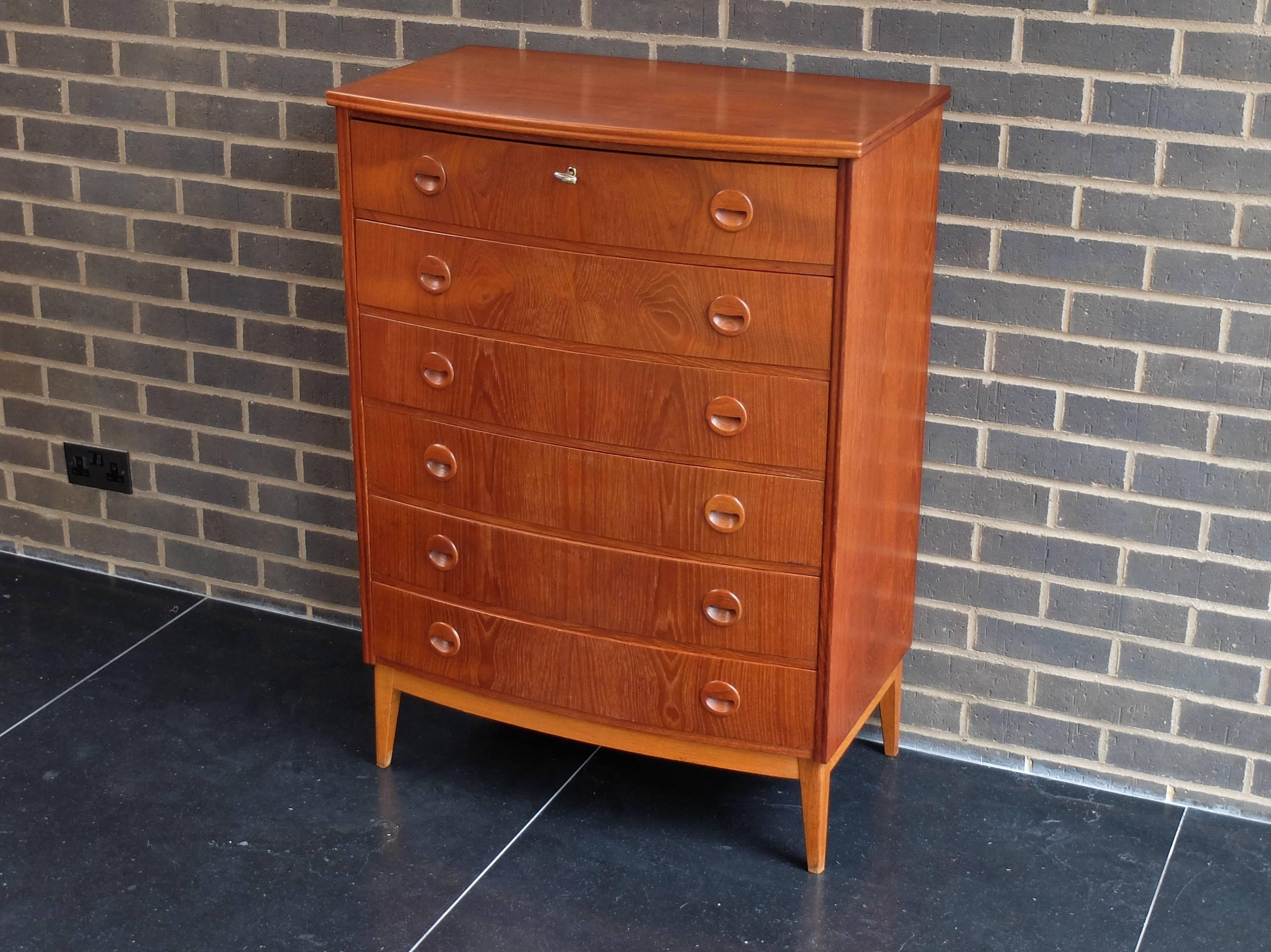 A Kai Kristiansen bow-fronted teak chest of drawers or dresser on contrasting oak legs and frame. The six drawer fronts are matched and have recessed teak pulls. Top drawer is locking and has working key. Produced in Denmark in the 1960s.