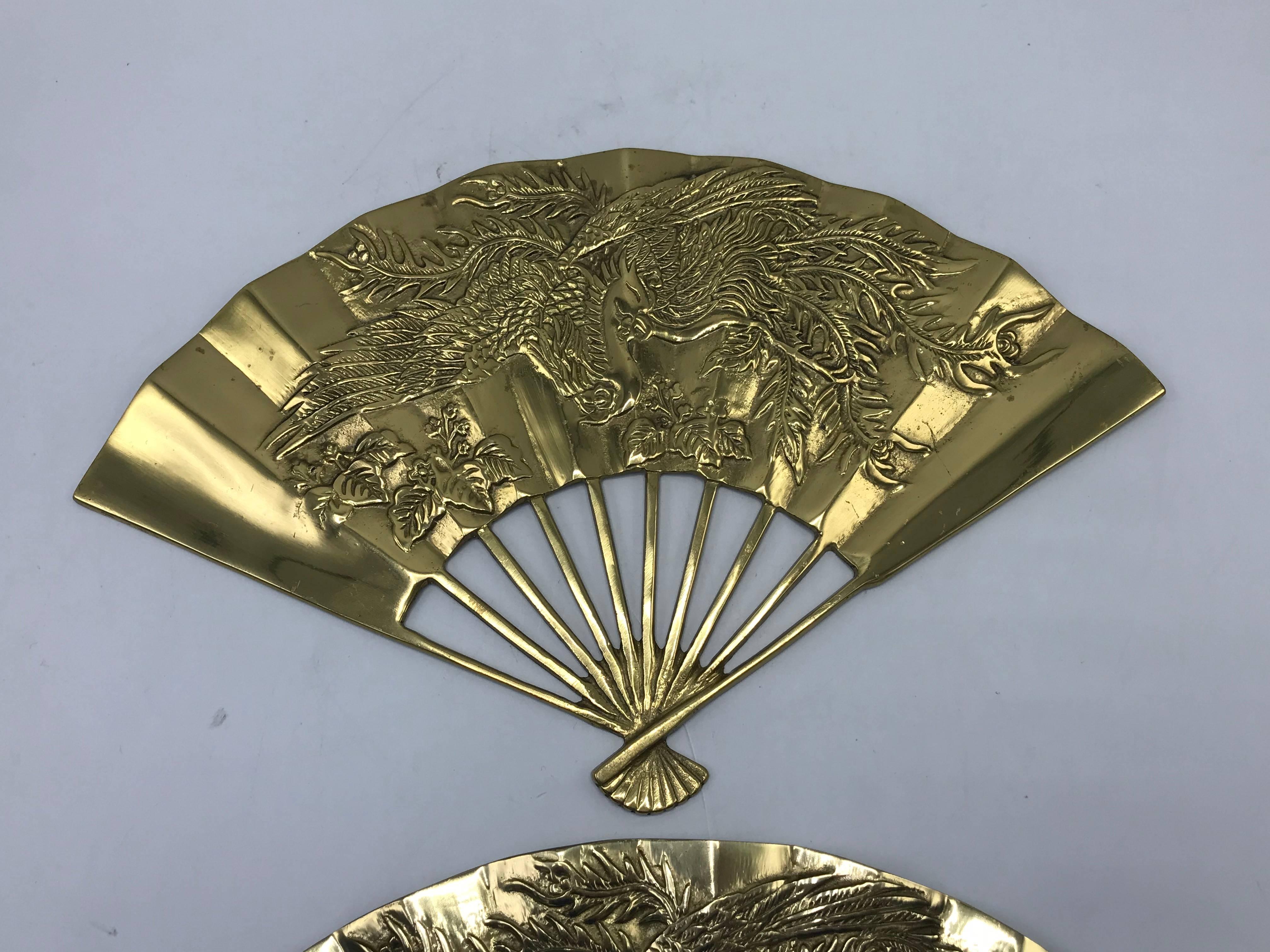 Listed is a gorgeous, pair of 1960s solid-brass chinoiserie wall sculptures in the shape of hand-fans. Each have matching, ornate dragon motifs. Wall hooks on backside for easy hanging. Heavy.
