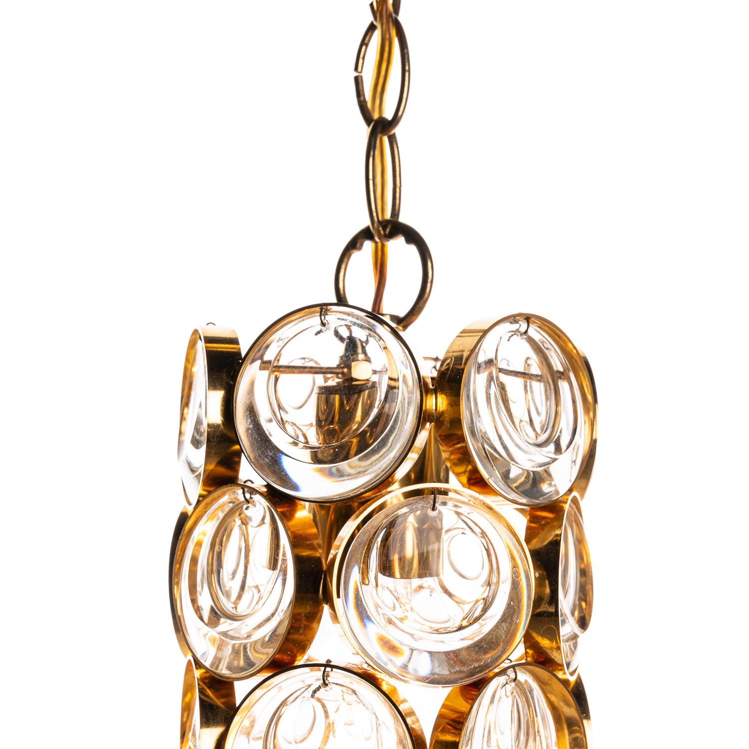 Petit pendant by Palwa. Consist of a gilded brass frame & rings with crystal Glass “lenses”. It holds one E27 socket and is in excellent condition. 
Large chandeliers, wall lights and pendants.
