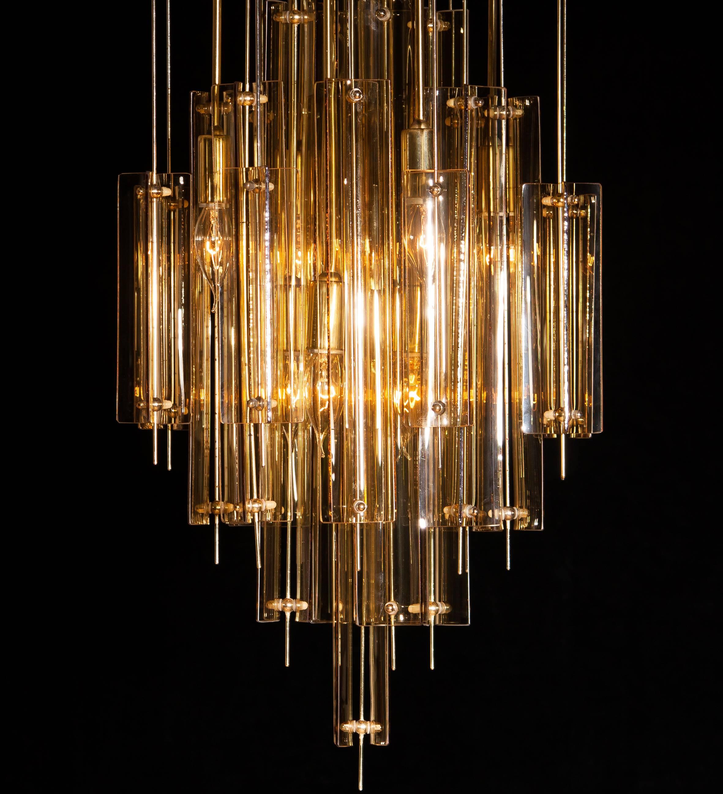 Amazing chandelier in the manner of Verner Panton.
This lamp is made of a gold lacquered metal ceiling plate with brass and fumé glass elements.
It is in a very nice, fair to age, condition.
Period 1960s.
Dimension: Total height 101 cm, ø 41 cm.