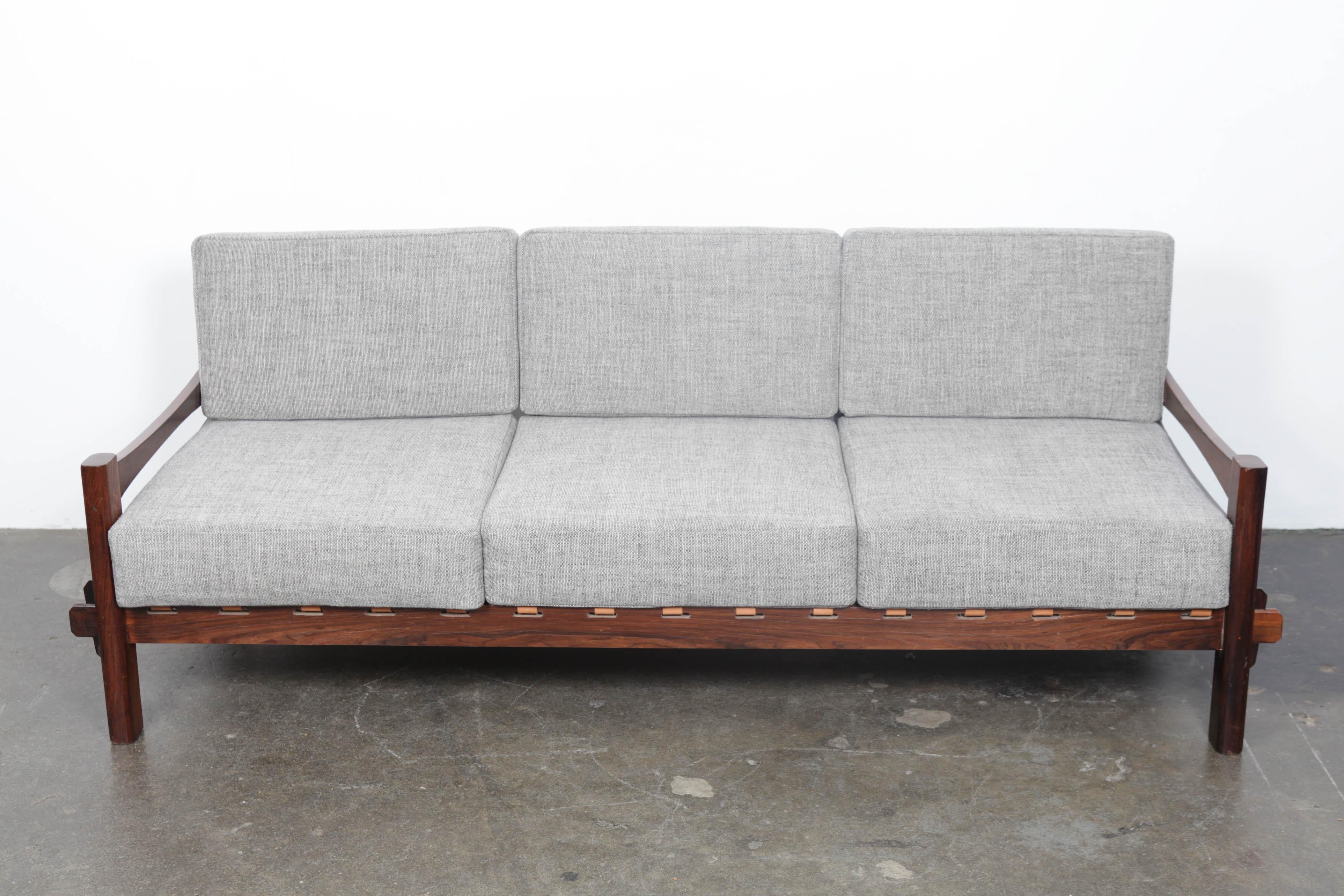 Unique solid rosewood 1960s Brazilian sofa with leather strapping and newly upholstered loose cushions in a light grey woven fabric. Designed unknown.
