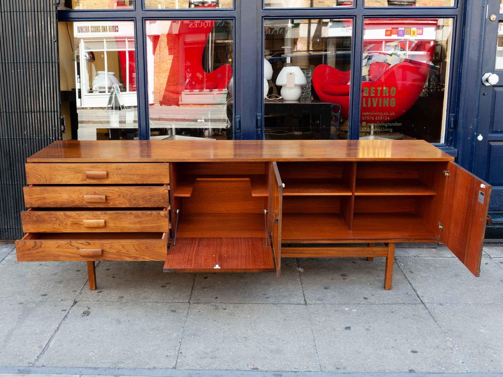 A stunning 1960s rosewood sideboard by British manufacturer Bath cabinet makers. The sideboard sits on a solid rosewood frame and features a two door cupboard for storage, a single pulldown drinks bar section and a set of four drawers. The cupboard
