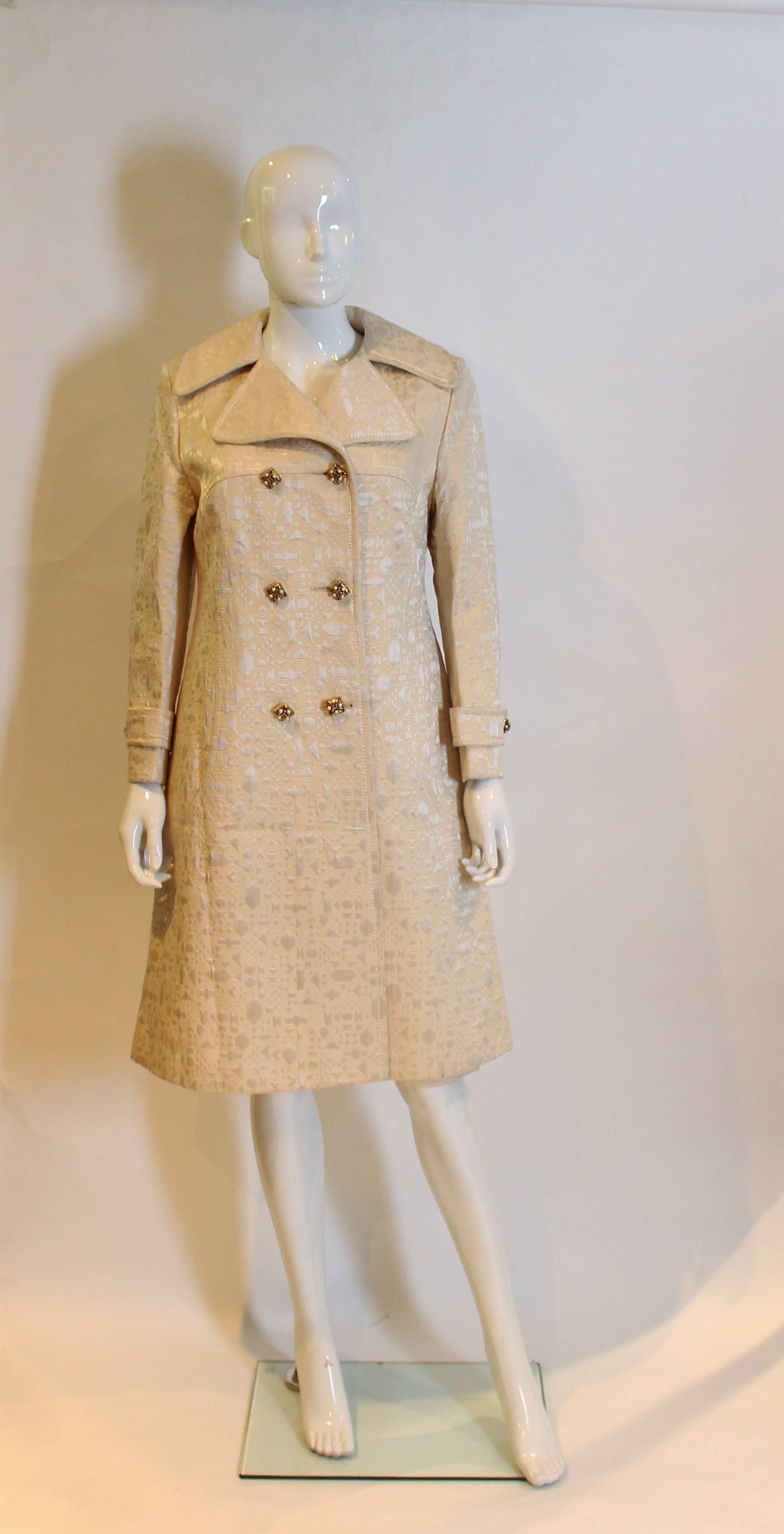 A chic coat by Braucschweig of Switzerland, made for the department store, Browns of Chester. The coat is made of a cream coloured, brocade like fabric with 6 buttons on the front, one on each cuff and a cut away collar.