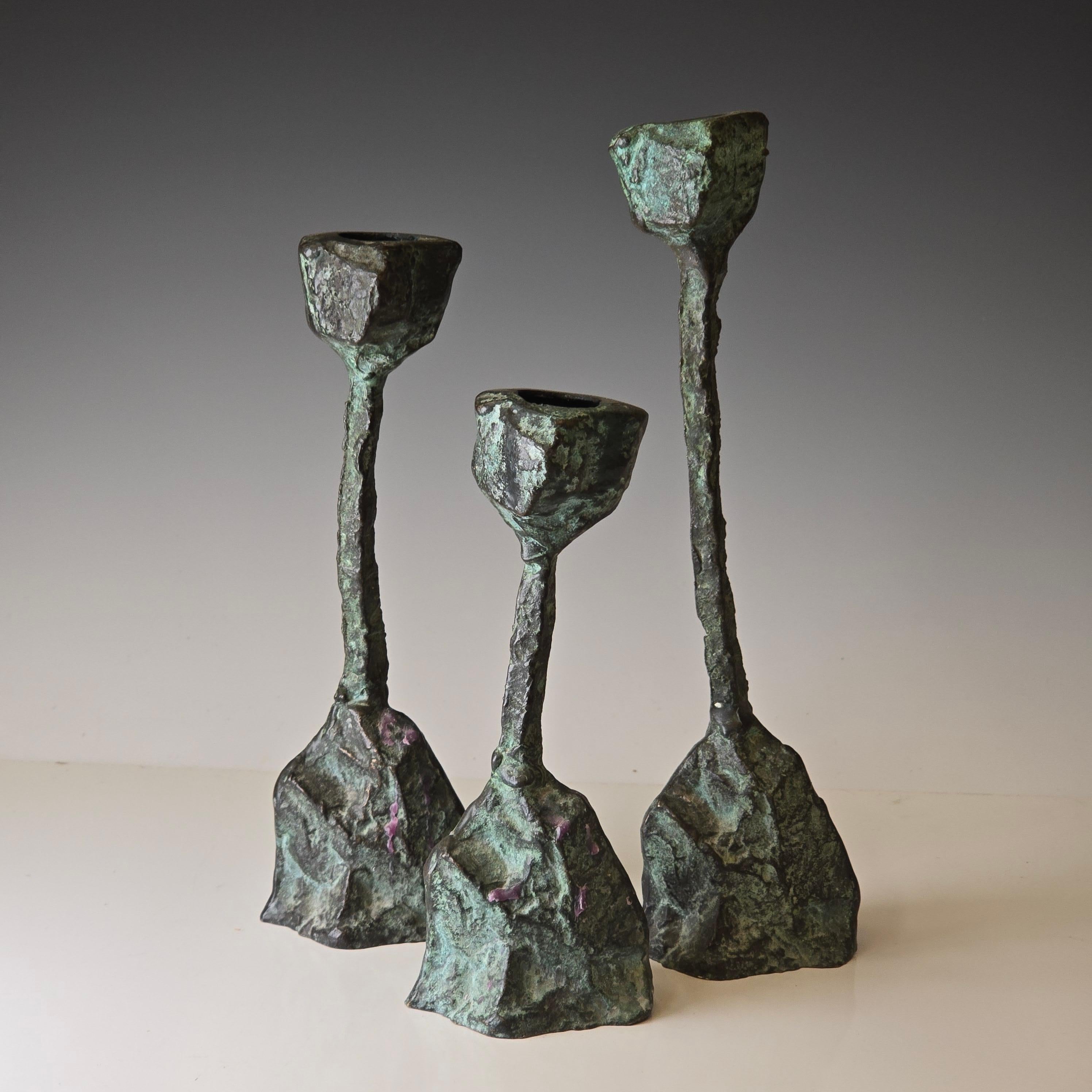 A trio of cast bronze brutalist candlesticks from the 1960s with beautiful verdigris patination and some worn spots thay have darkened with natural age.   Size is for the largest, the medium is 8 inches tall and the small is 6.5 inches tall with a