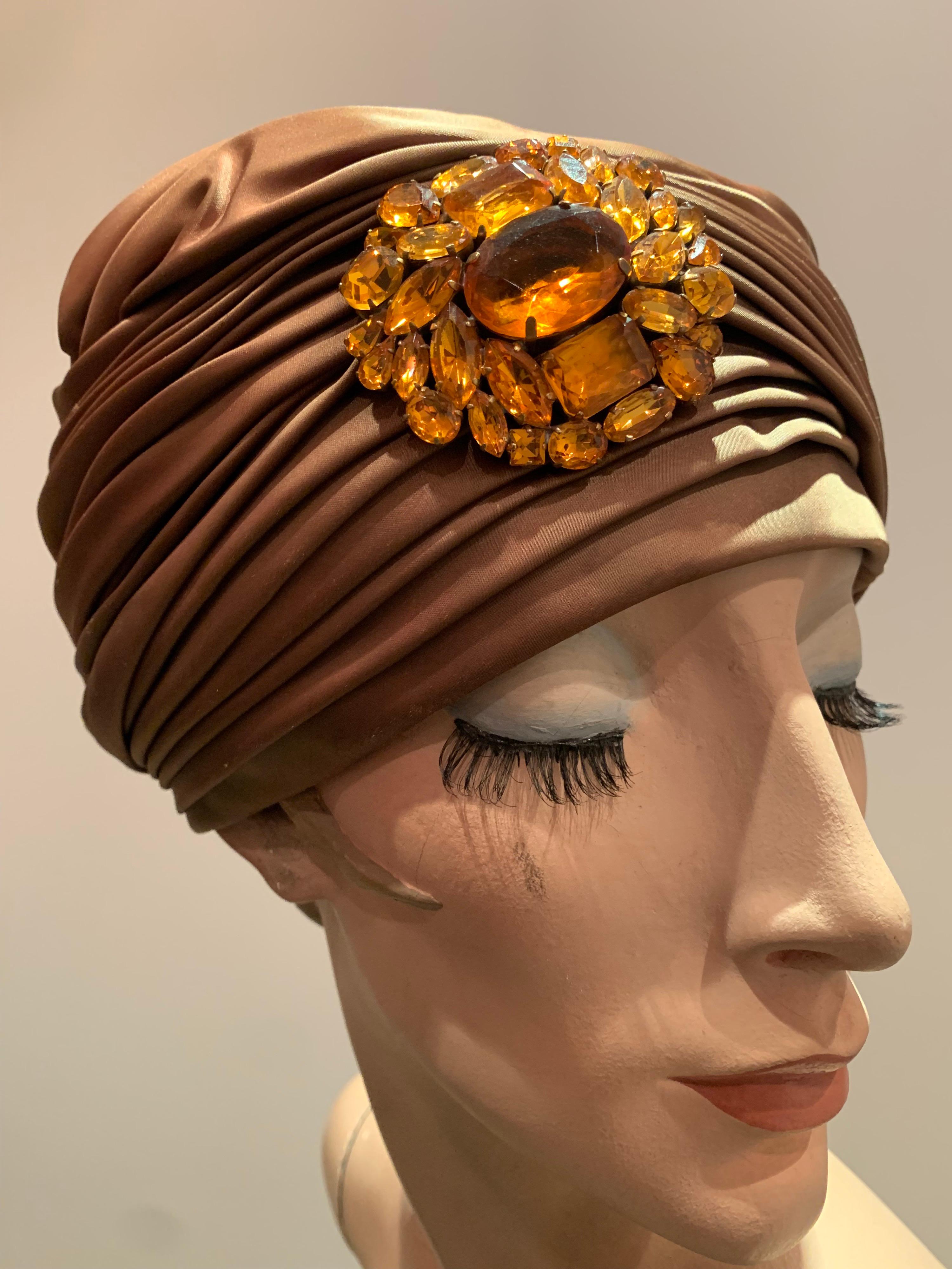 Ein unmarkierter Turbanhut aus bronzenem Satin der 1960er Jahre mit einer großen Strassbrosche mit Cabochon.  