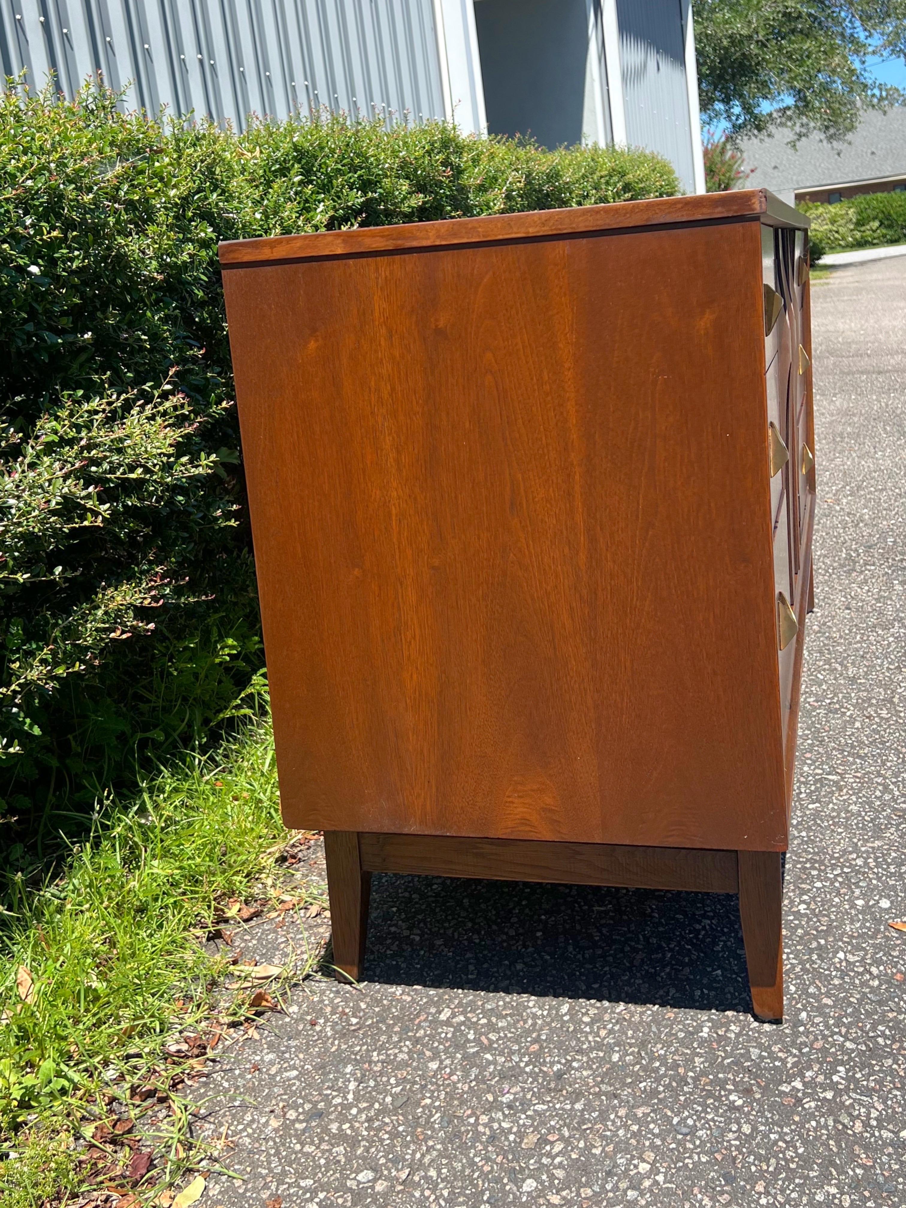 An iconic Broyhill Brasilia Mid-Century Modern sculpted walnut nine-drawer dresser. The dresser features gorgeous walnut wood grain, with sculpted arches and original pulls. The center sculpted cabinet doors open up to three drawers with an