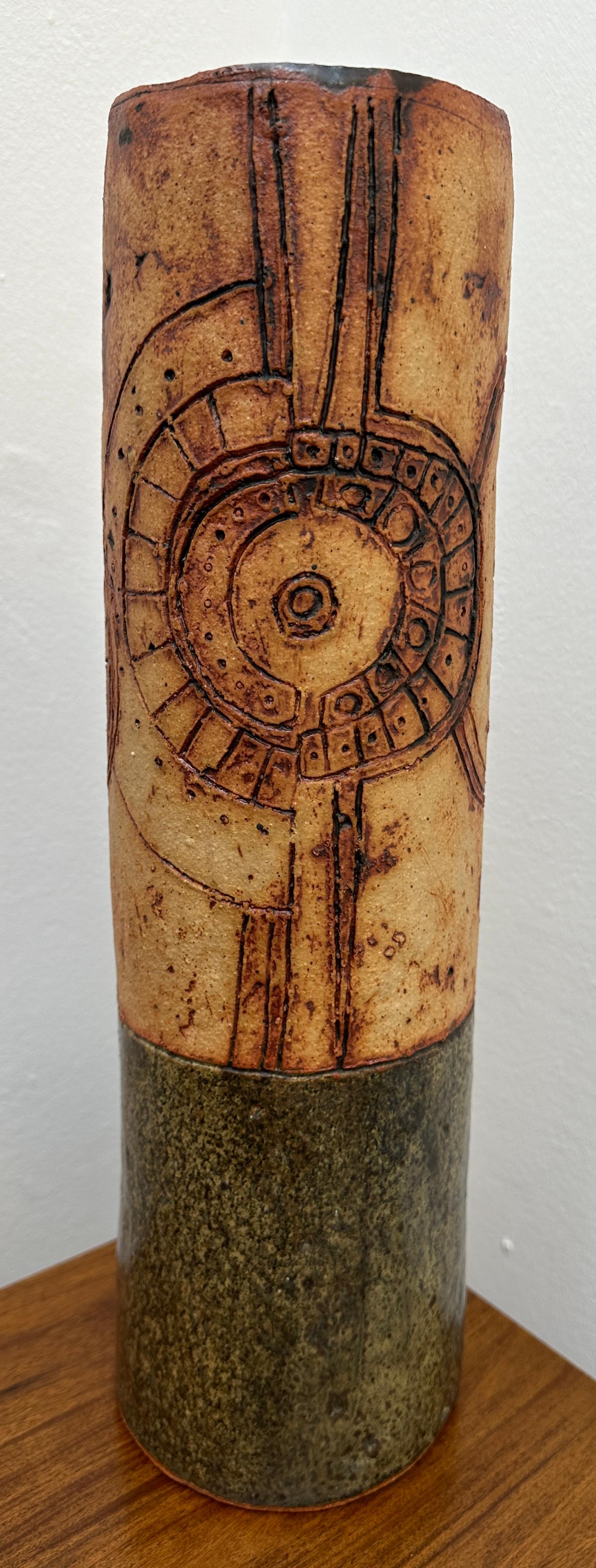 A large 1960s vintage Studio Pottery early brutalist cylindrical ceramic vase by British ceramicist Bernard Rooke.  The upper two-thirds features an incised abstract design which is reminiscent of a clock face and its inner workings in hues of