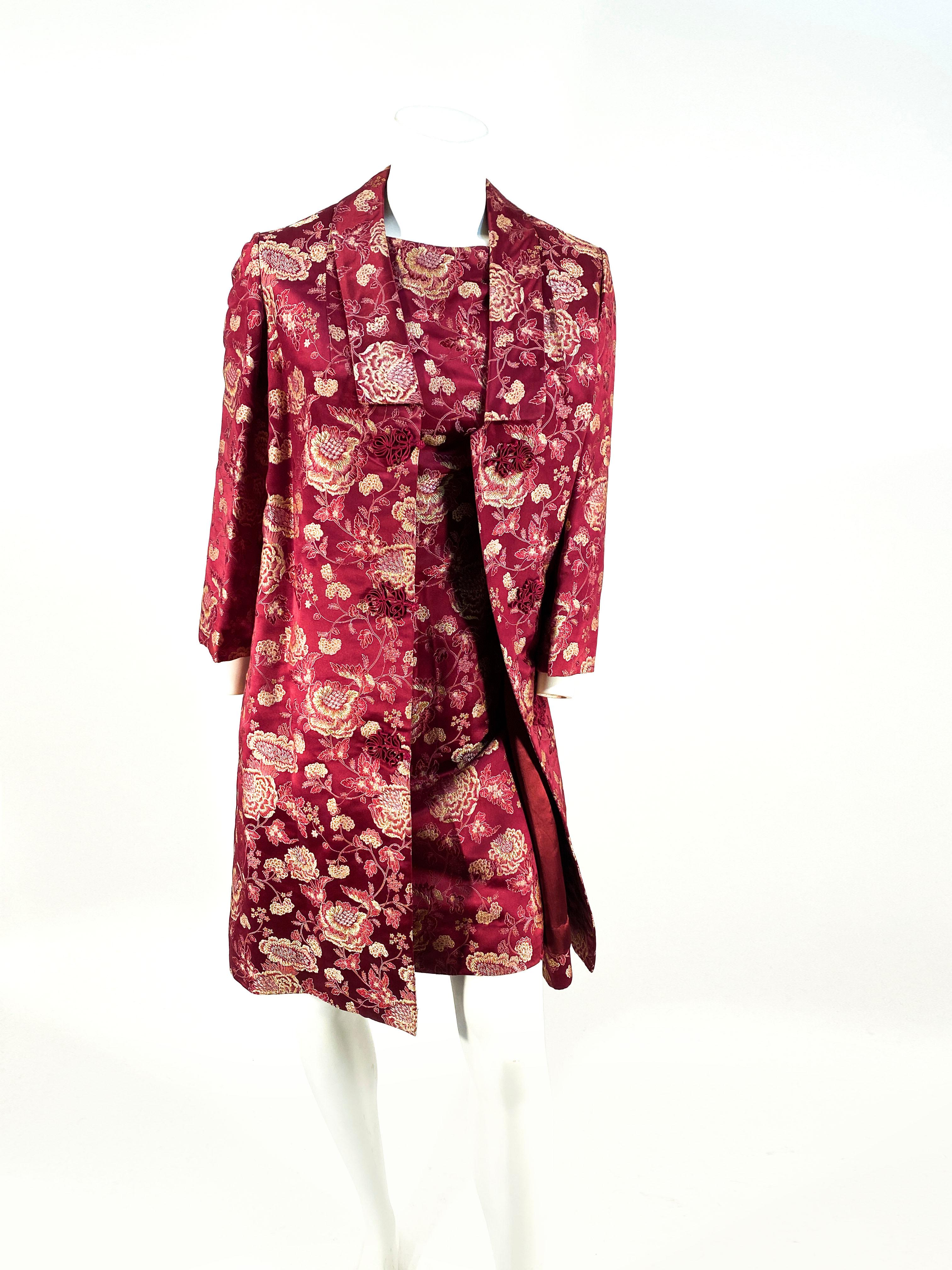 1960s Burgundy and floral brocade custom-tailored shift dress with a matching glove length sleeved coat. The coat is fully lined with interior and exterior pockets, frog closures, and a simple short shawl collar. 